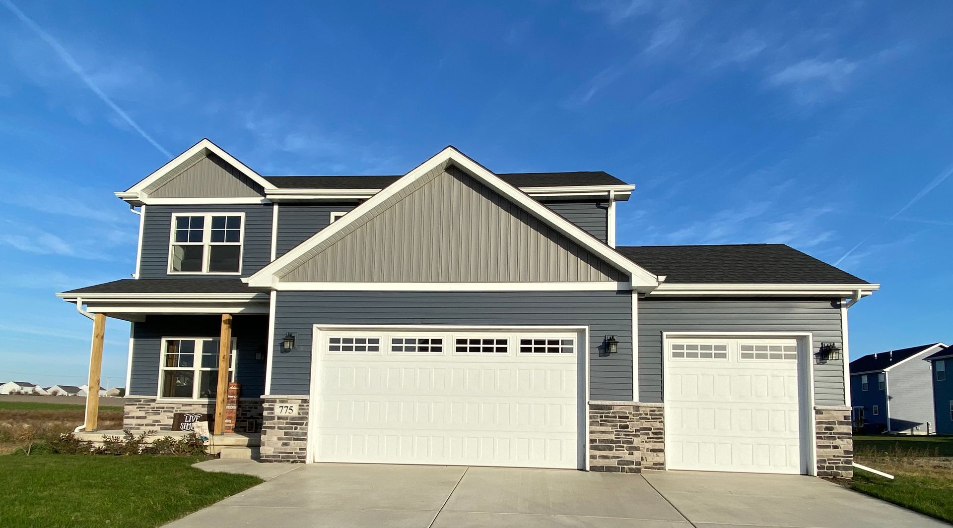 Blue two-story suburban house with white trim, double garage, and stone entry on a sunny day