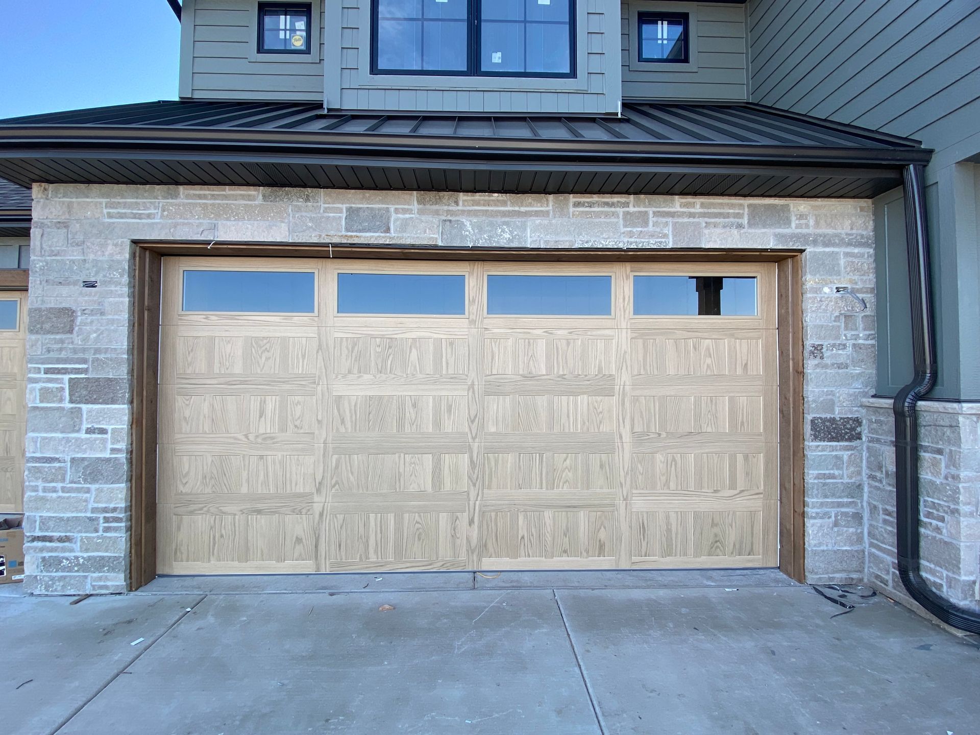 Wooden double garage door on a stone-faced house exterior with a concrete driveway
