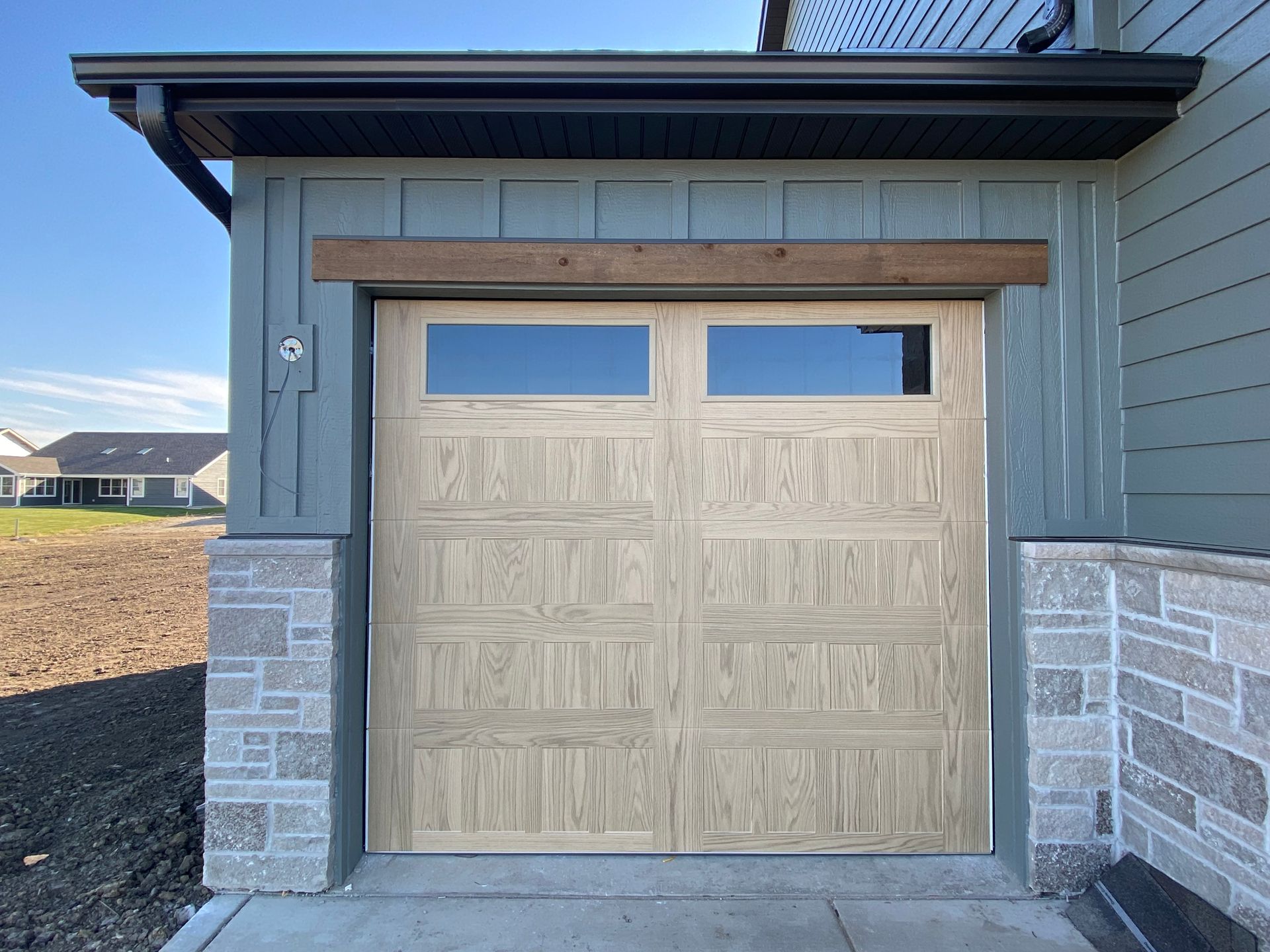 Beige garage door with two small windows on a gray-blue house exterior.
