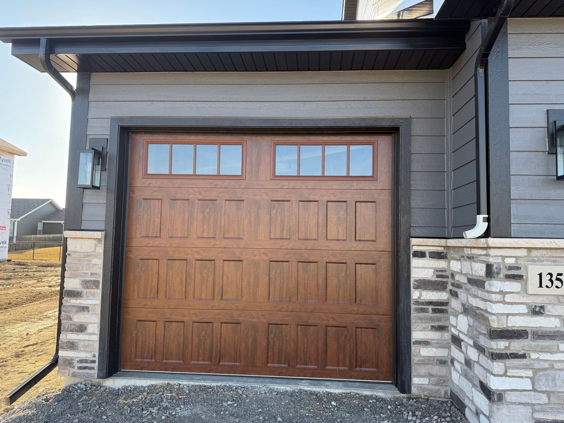 Closed wooden garage door on a modern house exterior with stone columns and gray siding.