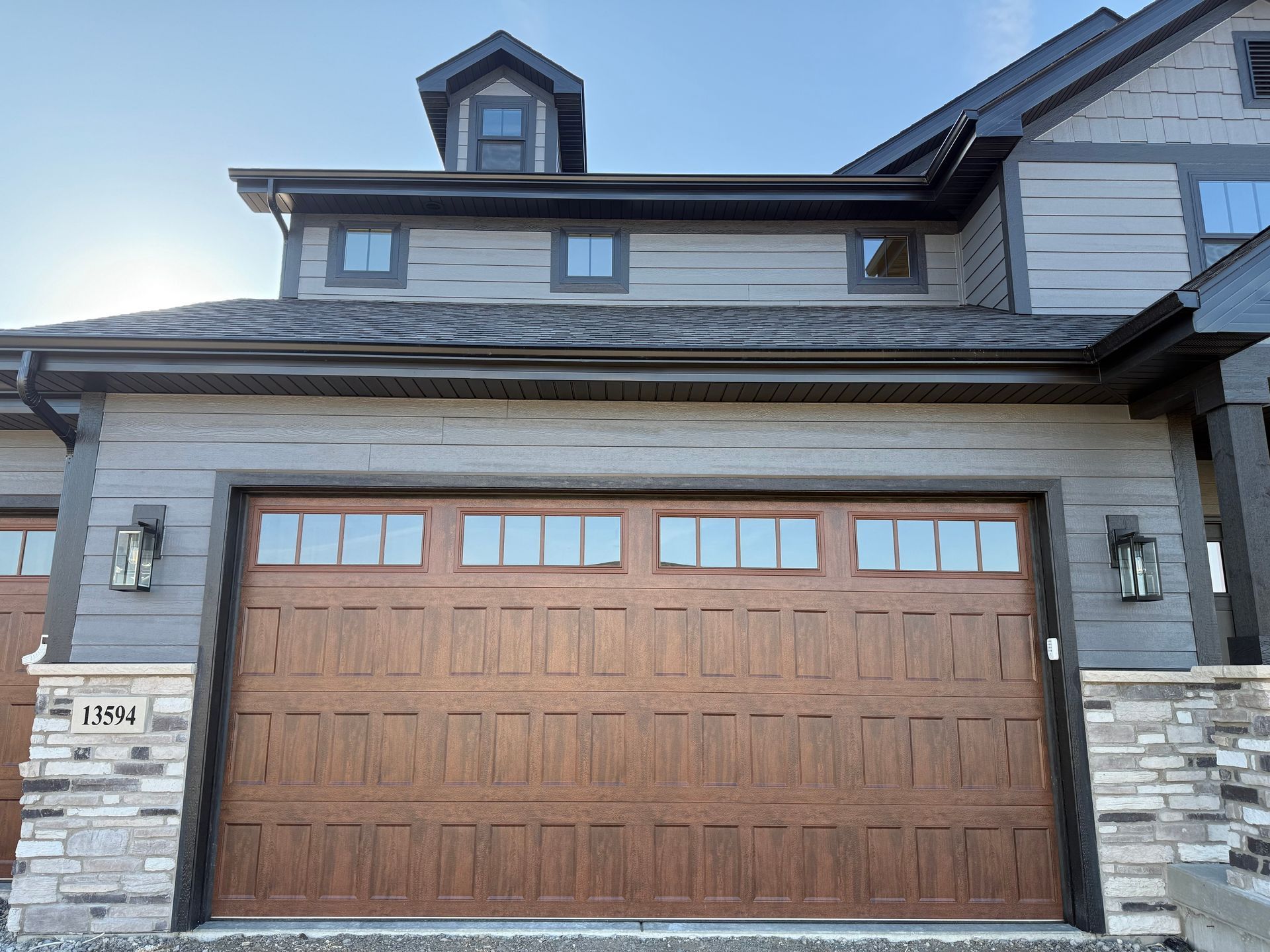 Front view of a modern house with a large wood garage door and stone siding