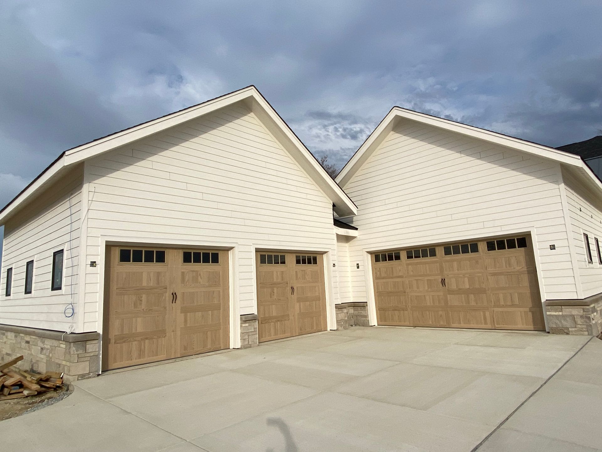 Two white garages with tan doors and a wide concrete driveway under a cloudy sky