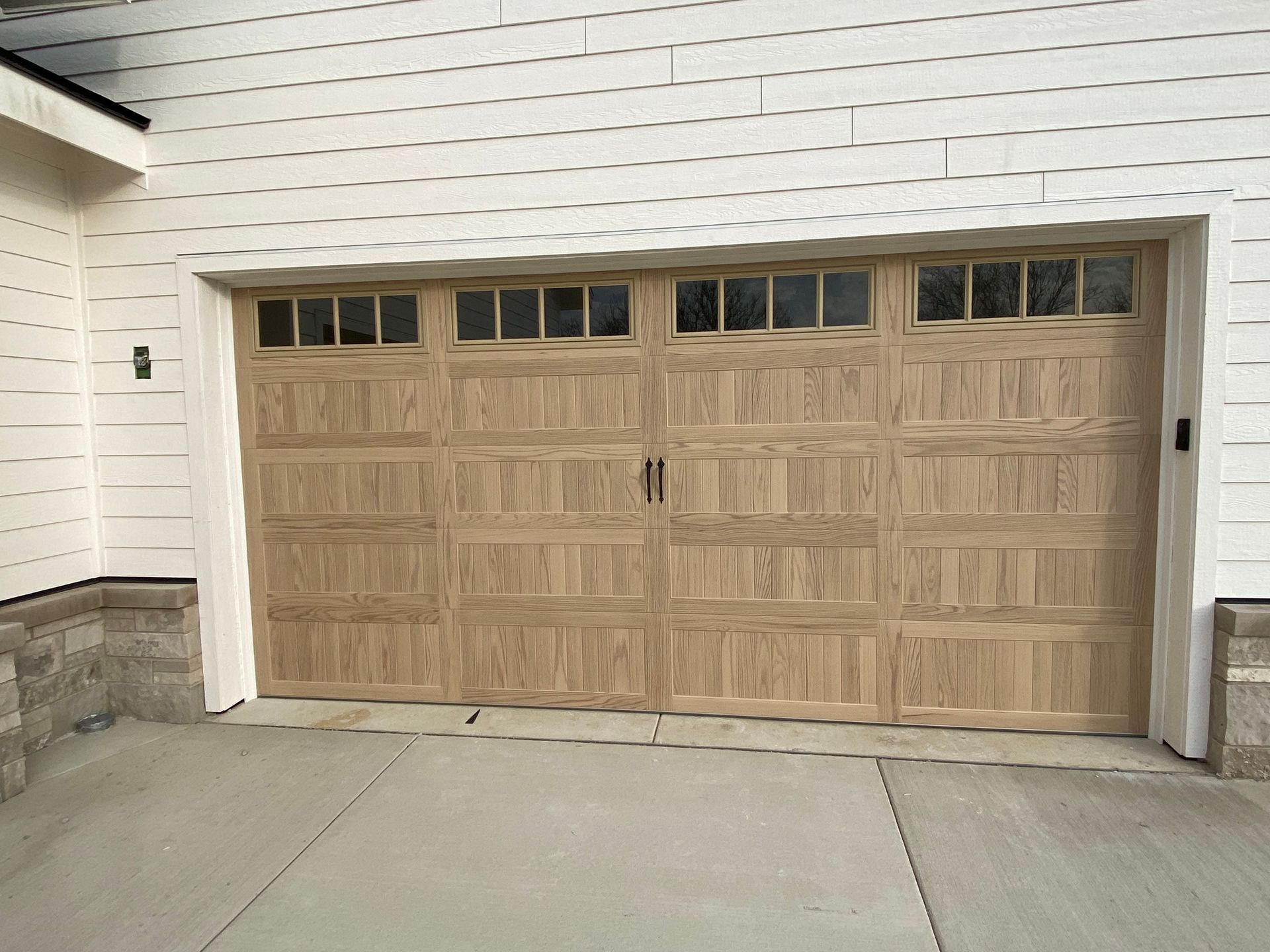 Wooden double garage door on a white house with stone trim and driveway in front