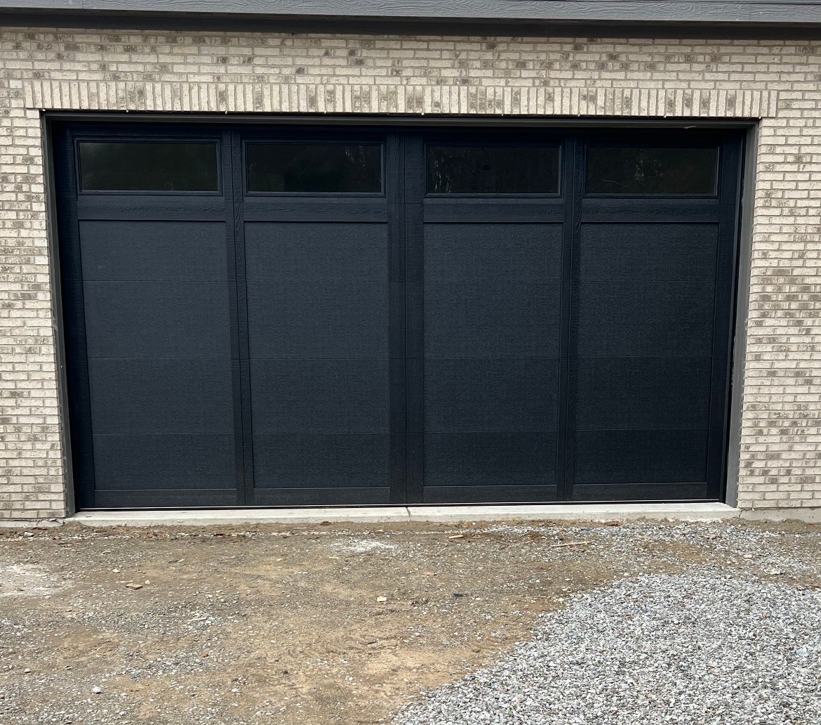Black metal garage door set in a light brick wall above a gravel driveway