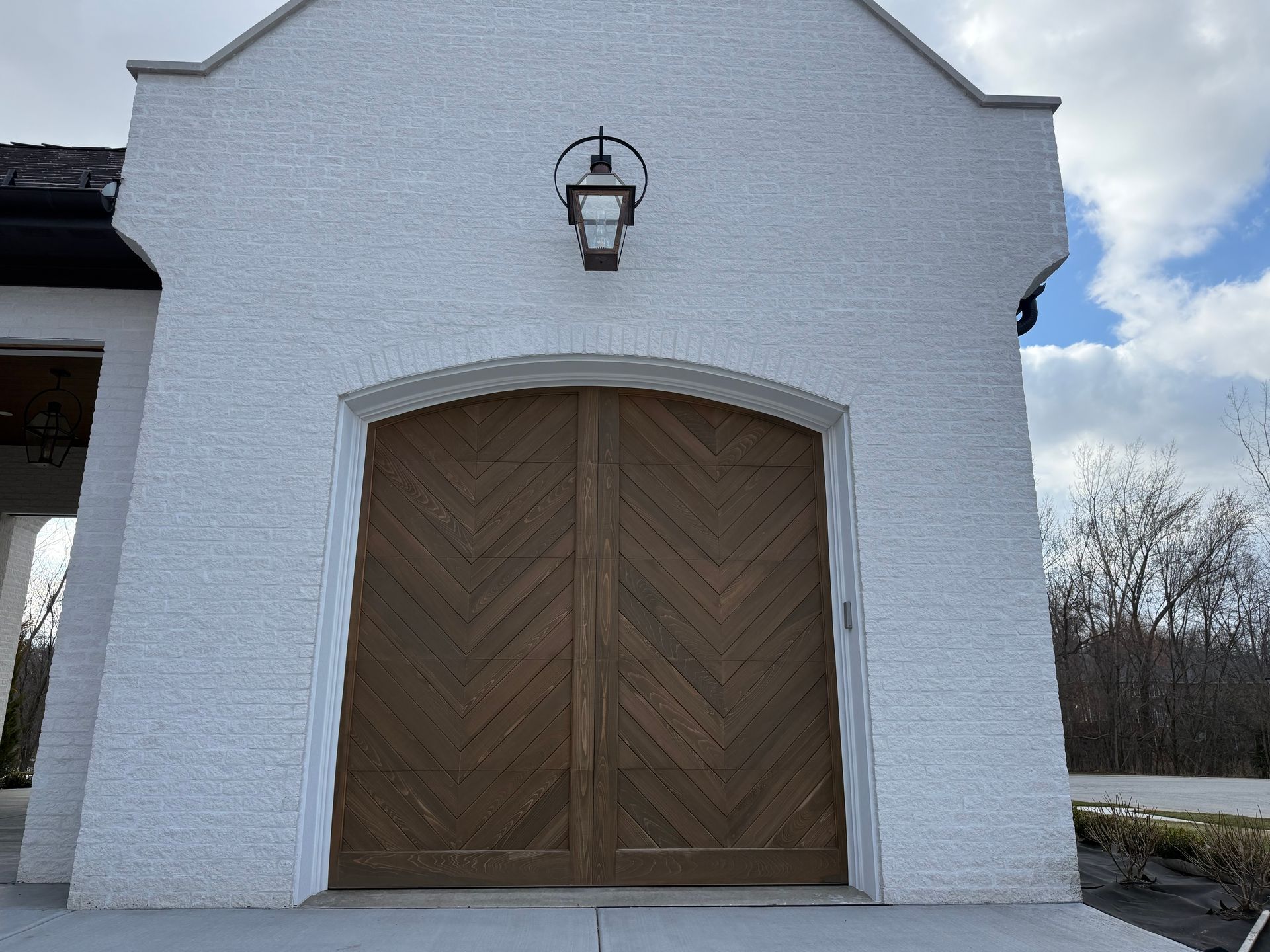 White brick building facade with arched wooden double doors and a lantern above the entrance