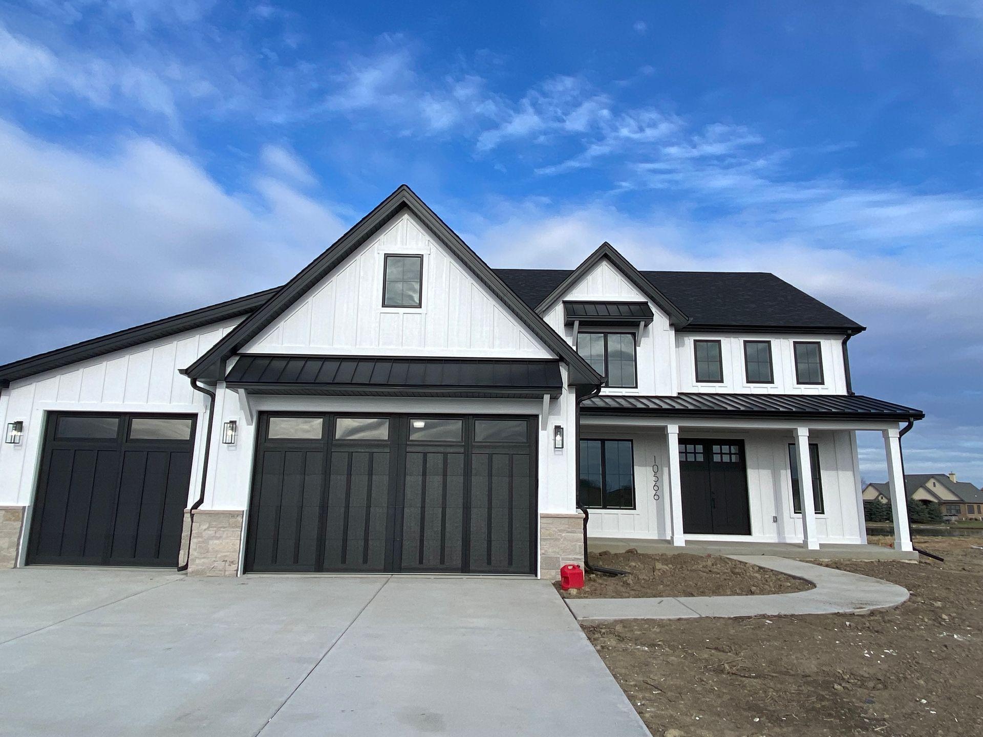 White suburban house with black garage doors, porch, and blue sky overhead