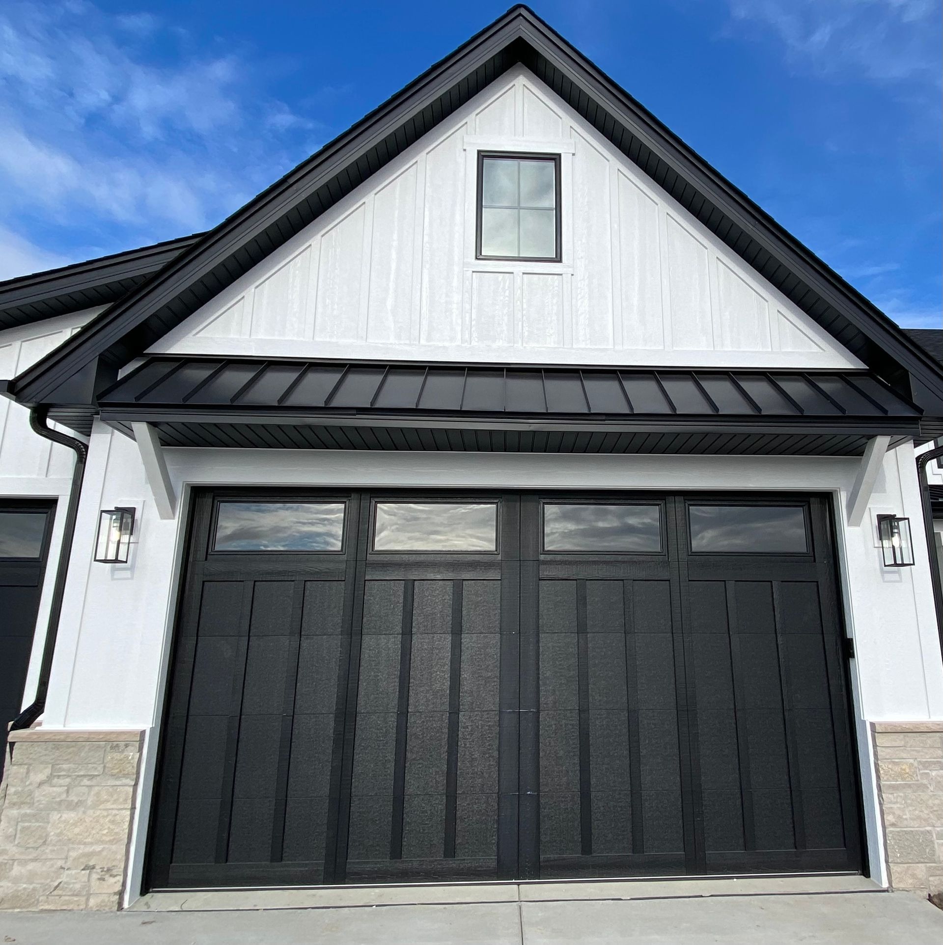 Modern black garage doors on a white house with a peaked roof and stone accents