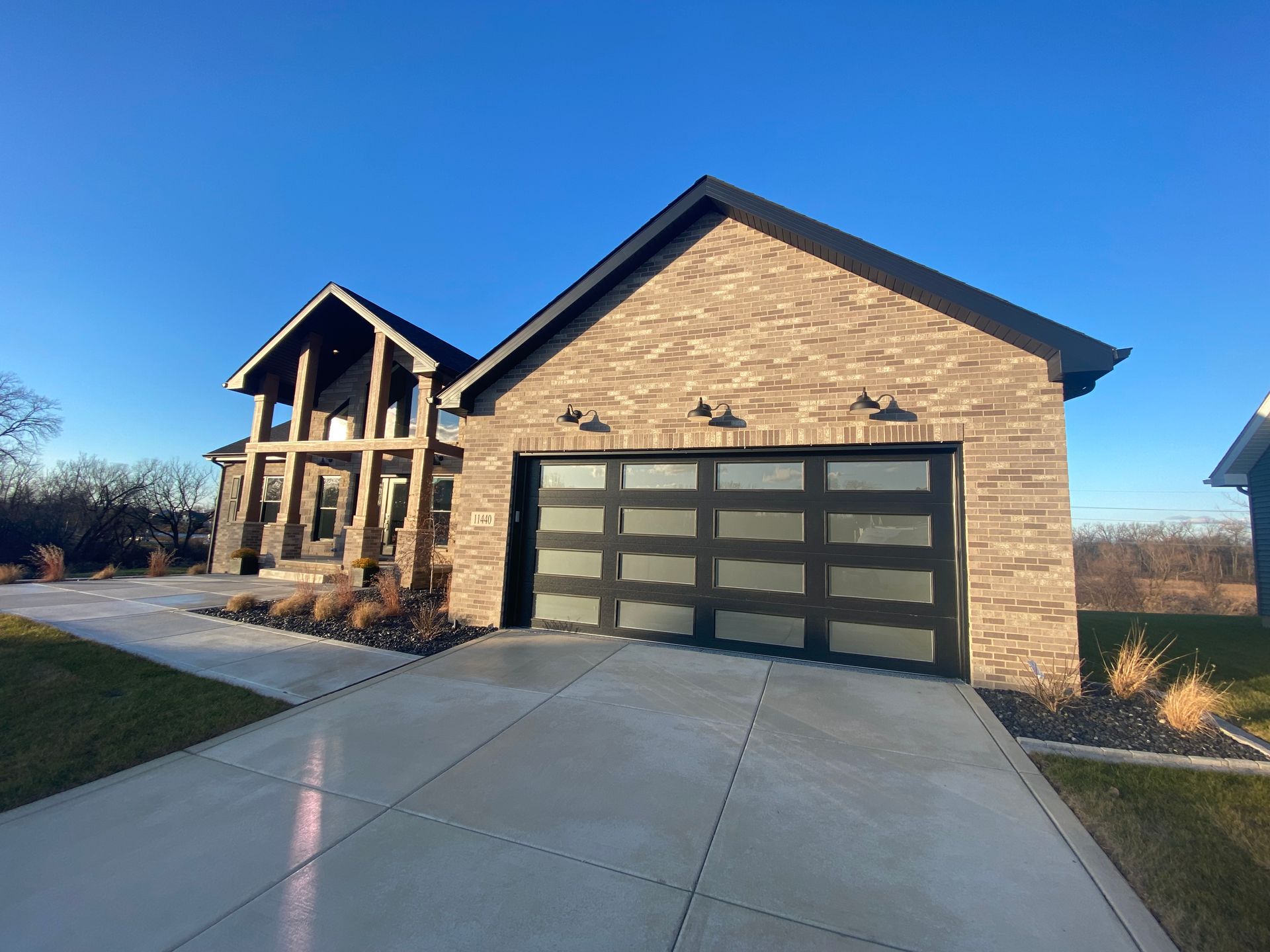 Brick two-story house with a three-car garage and a wide concrete driveway under a clear blue sky