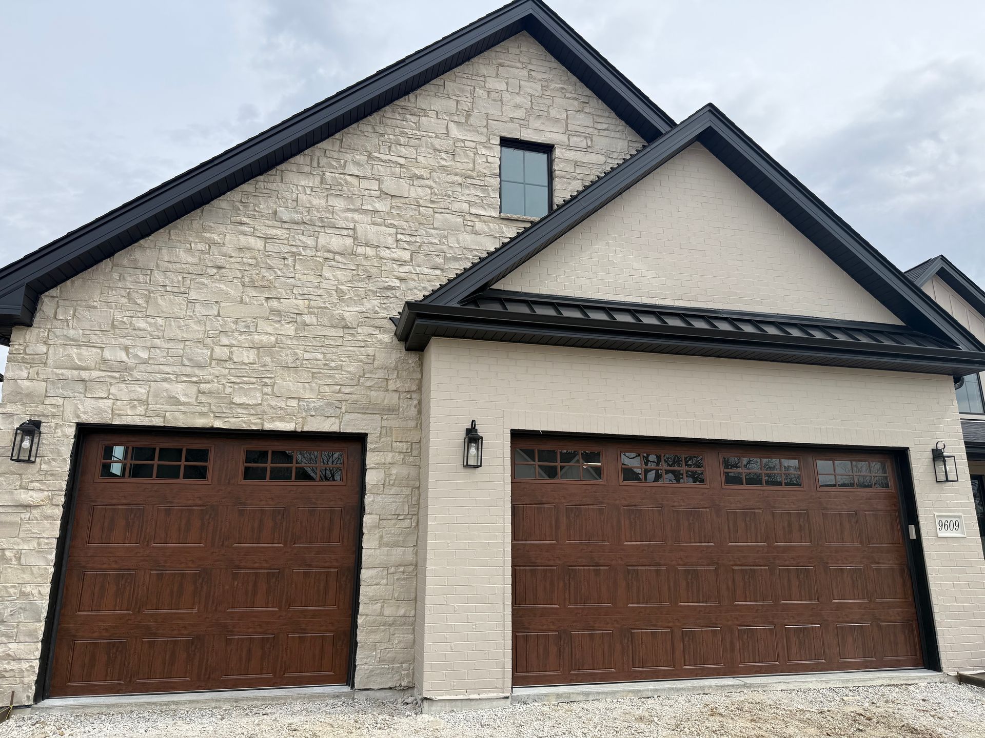 Front view of a stone house with two brown garage doors and black roof trim
