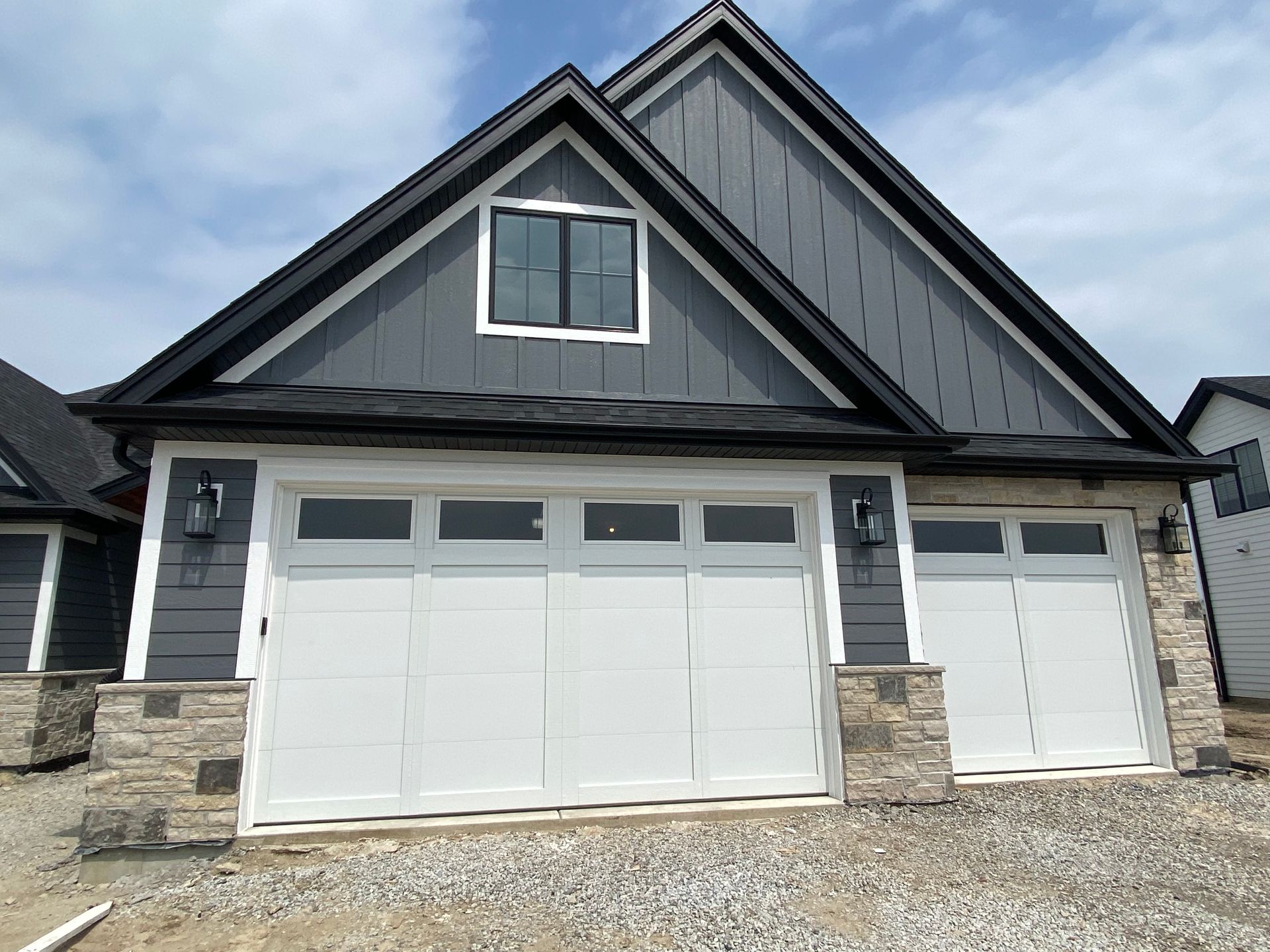 Gray two-story house with white garage doors and stone accents under a peaked roof.