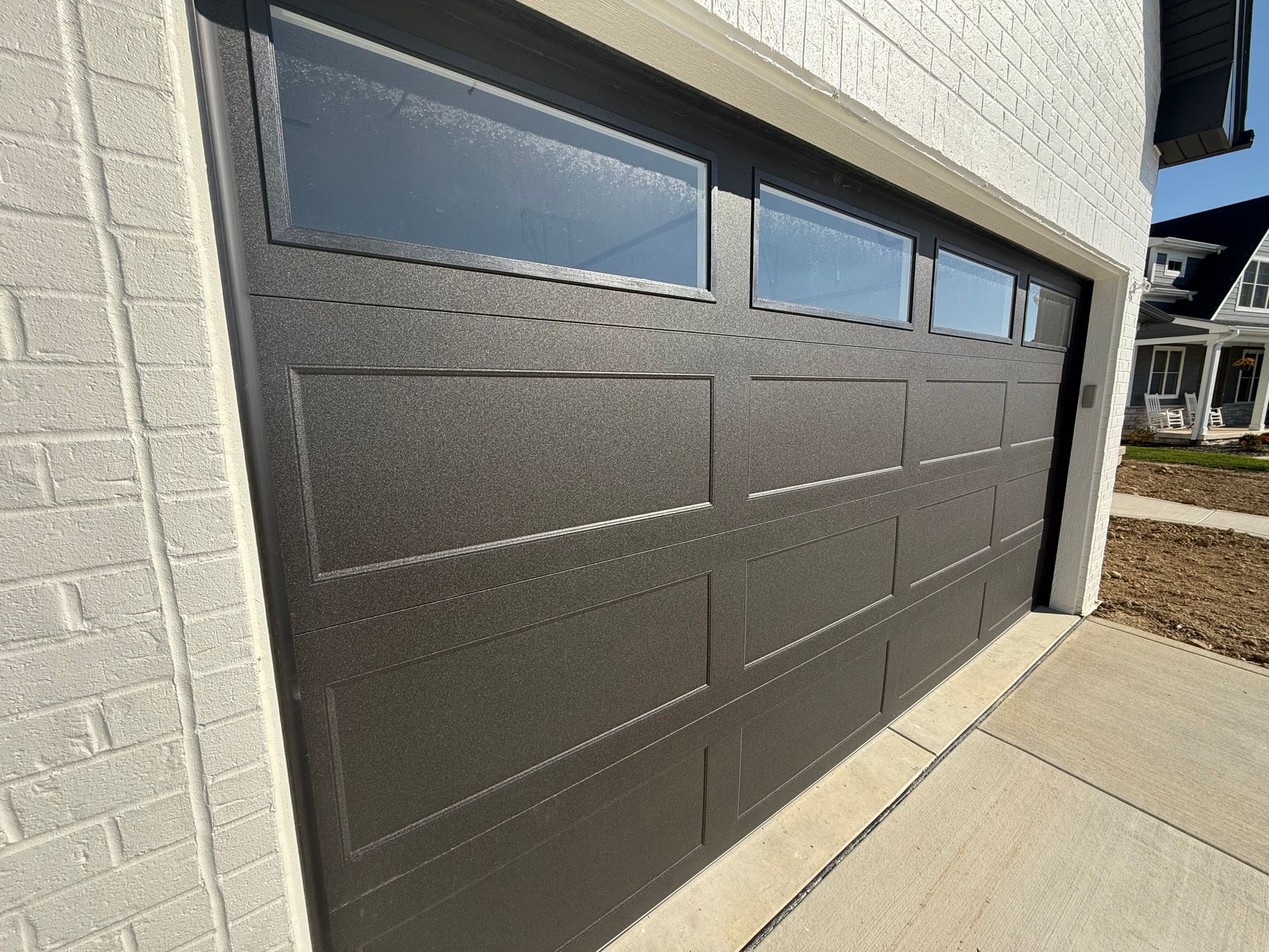 Dark gray modern garage door with narrow windows beside a concrete driveway.