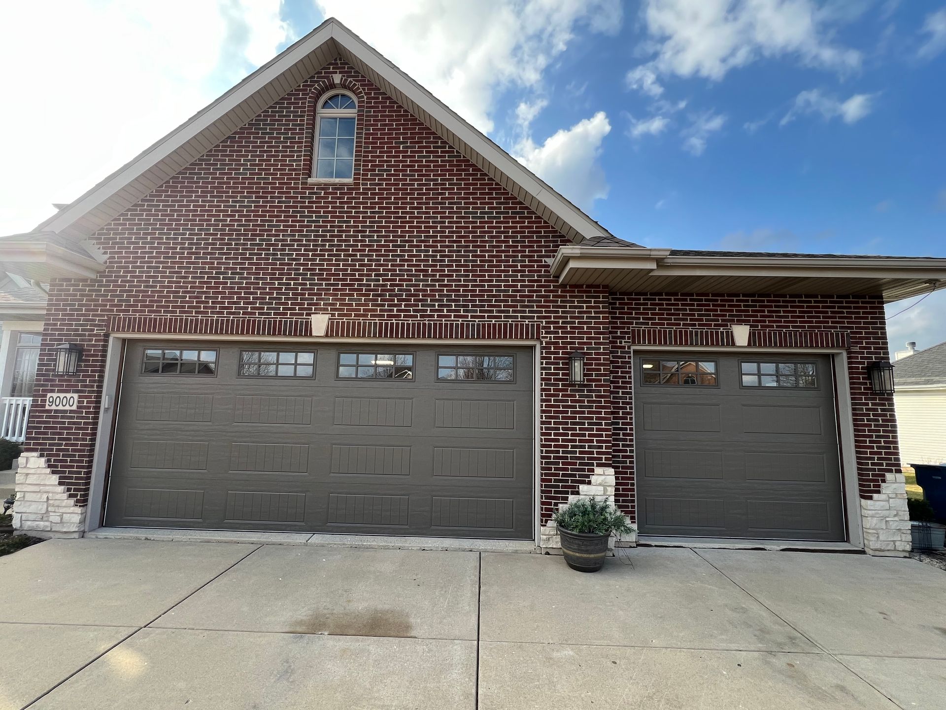 Brick house exterior with two gray garage doors and a small window, under a partly cloudy sky