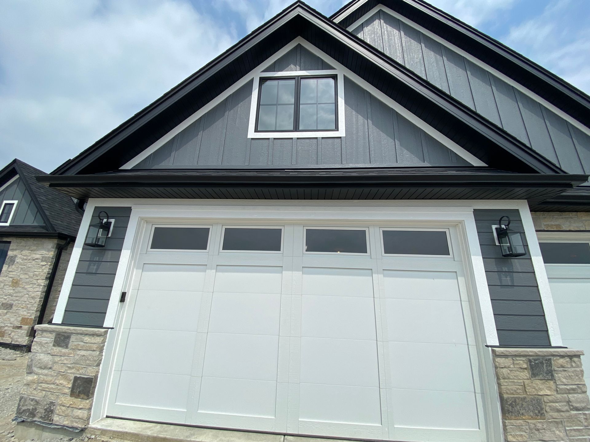 Front view of a gray house with a white double garage door and stone accents
