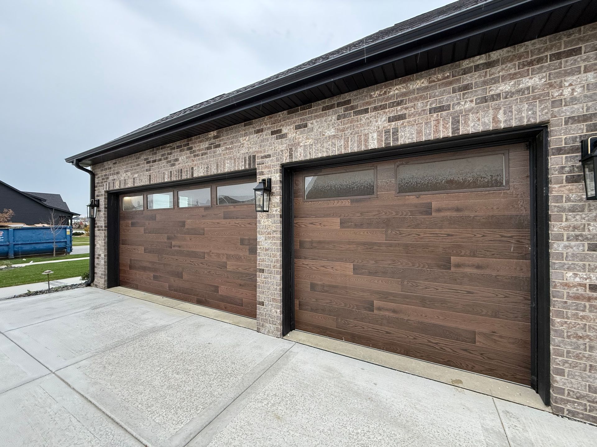 Brick garage with three wood-paneled doors and a concrete driveway under a black roofline