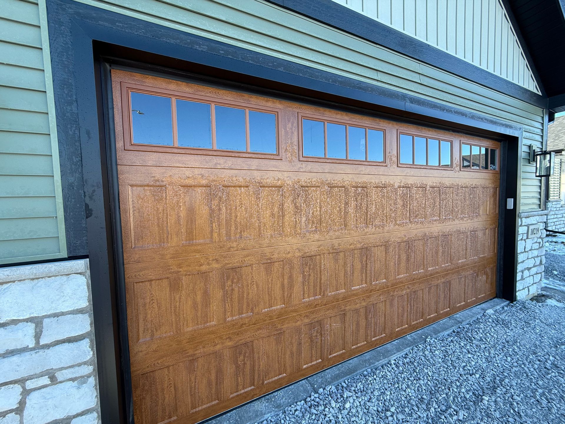 Wood-paneled garage door with small windows under a blue exterior, beside a stone wall.