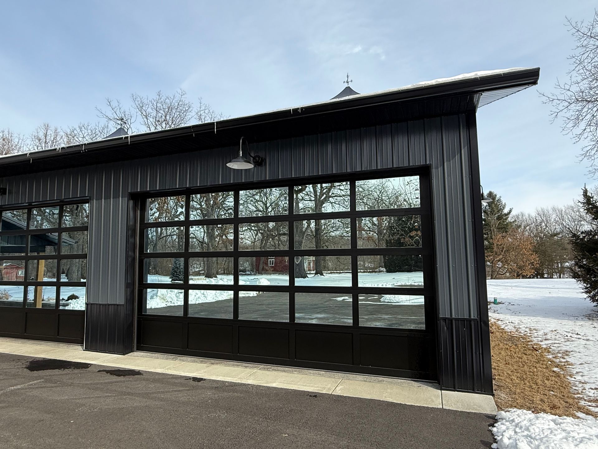 Black wooden building with large windows and a sloped roof beside a snowy landscape