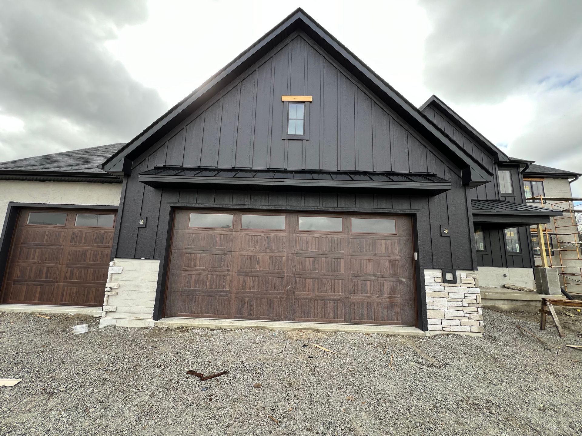 Black suburban house with a large garage and gravel driveway
