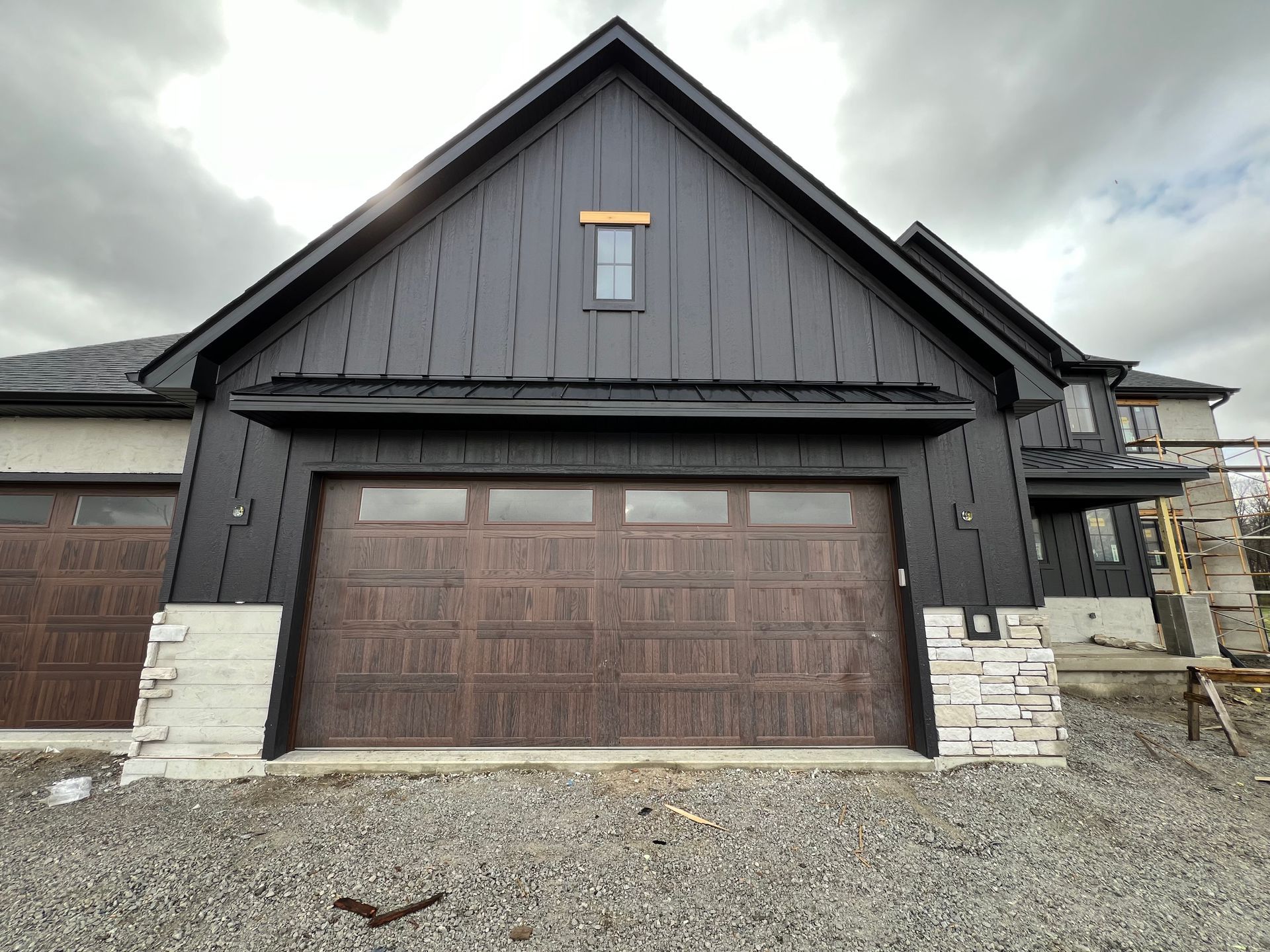 Front view of a dark gray house with a double garage and stone accents under cloudy skies