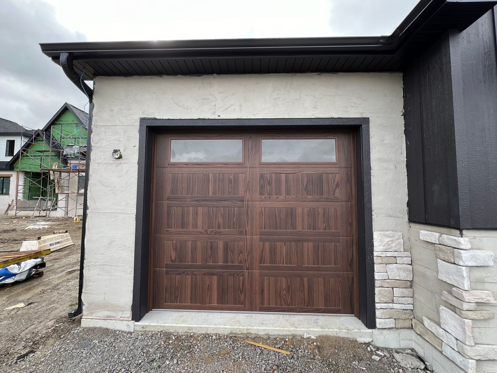 Wooden double garage door on a white and black house exterior under construction