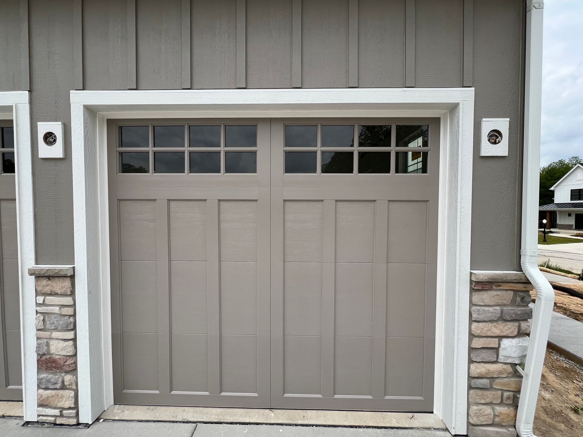 Gray garage door with white trim and stone accents on a house exterior