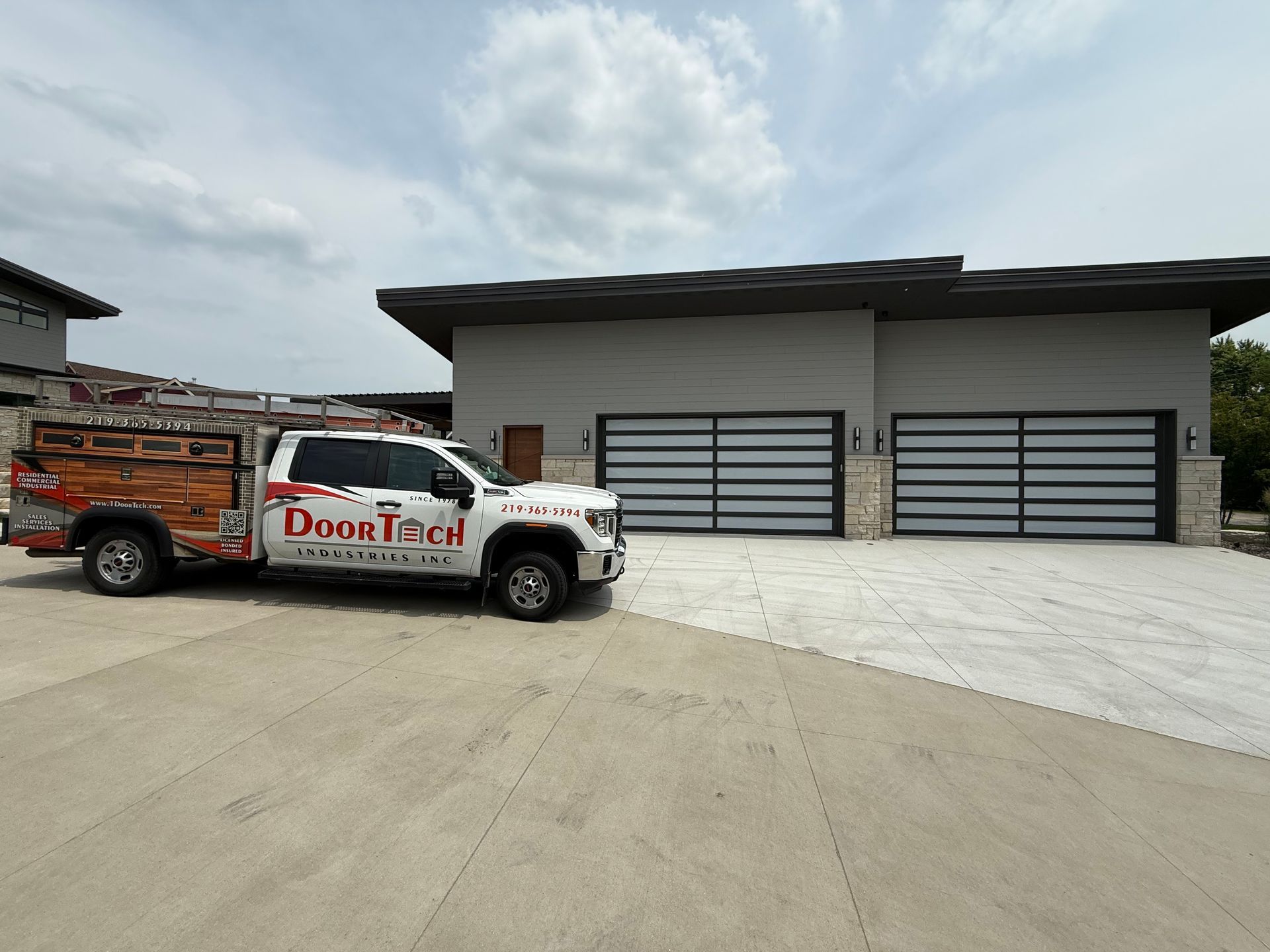 White DoorTec truck and trailer parked in front of a modern gray garage with three large doors.