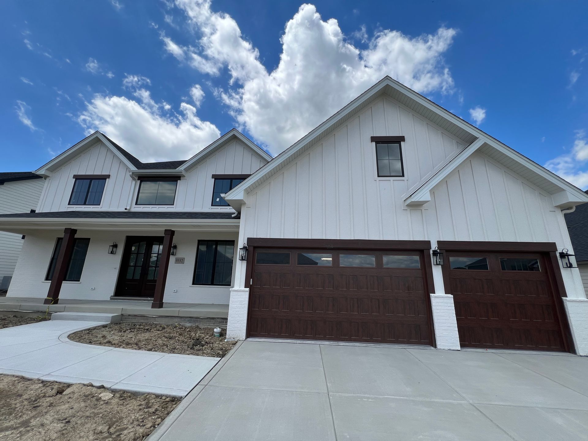 Suburban house with white siding, brown garage doors, and a blue sky with clouds
