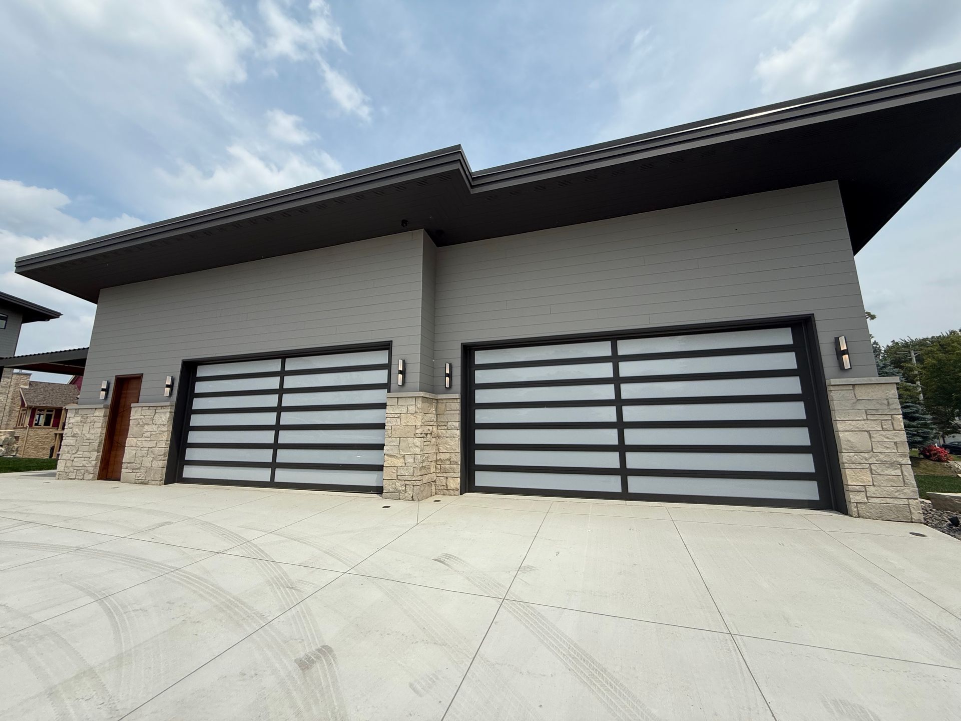 Modern house exterior with two gray garage doors and stone columns under a slanted roof