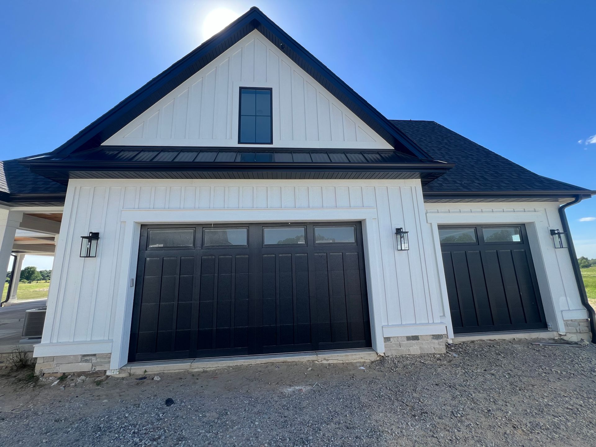 White house exterior with black garage doors and a steep dark roof under a blue sky