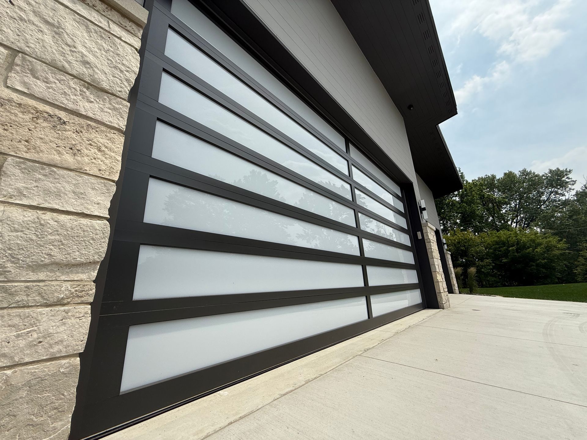 Modern garage door with frosted glass panels beside a stone wall and concrete driveway