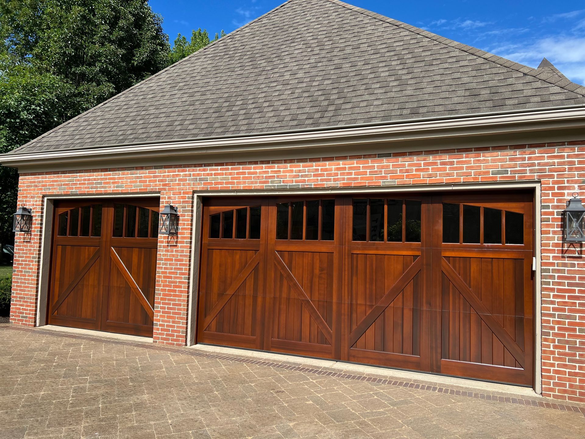 Brick garage with three wooden doors and a shingled roof in daylight