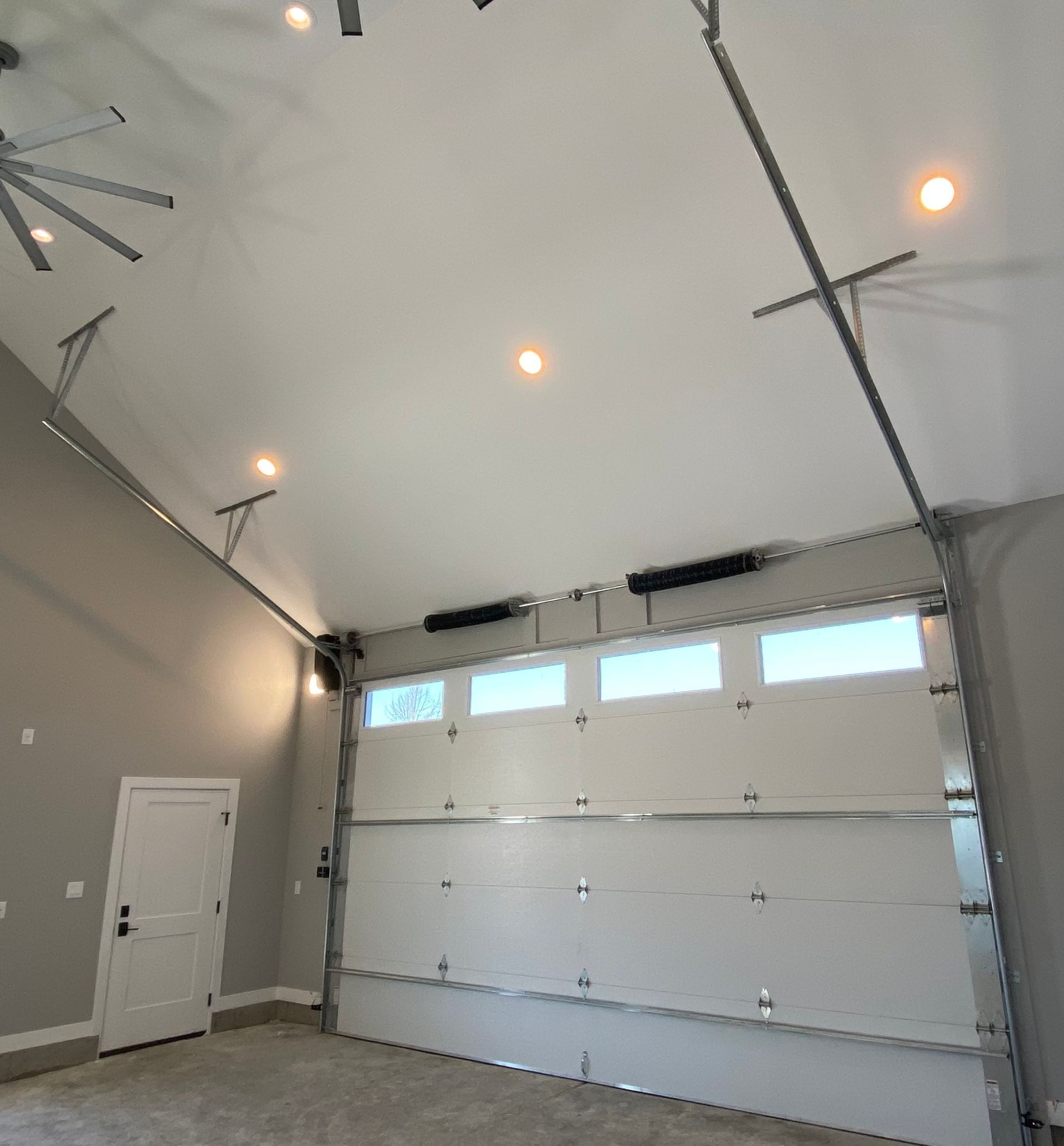 Empty garage interior with a large white overhead door and small high windows beneath a sloped ceiling.