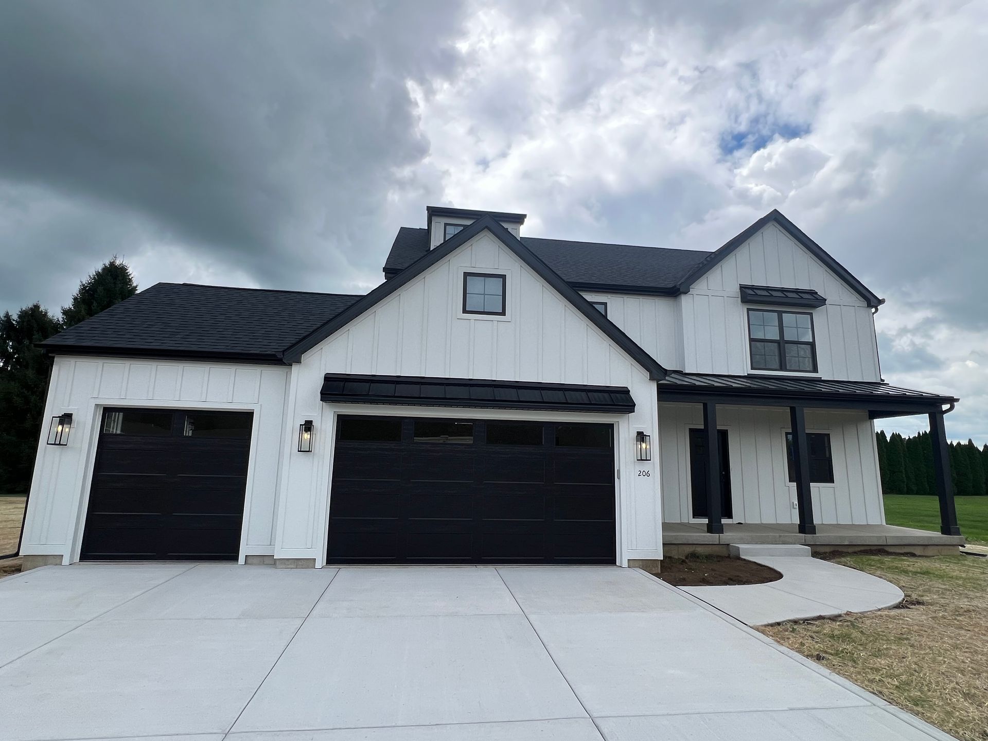 White modern house with black garage doors and driveway under cloudy sky