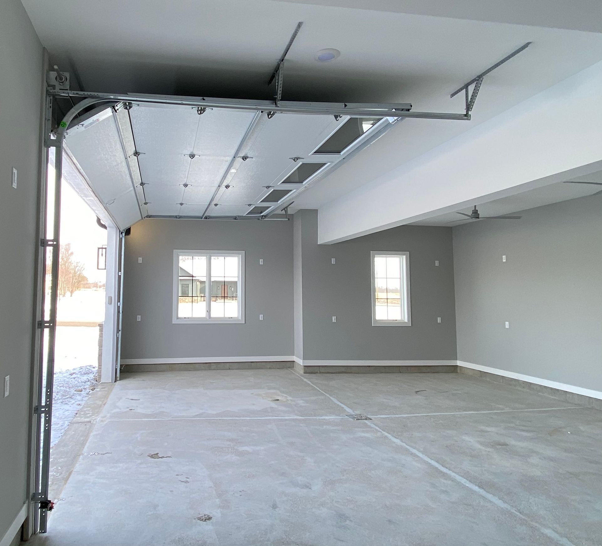 Empty garage interior with gray walls, concrete floor, and an open garage door.