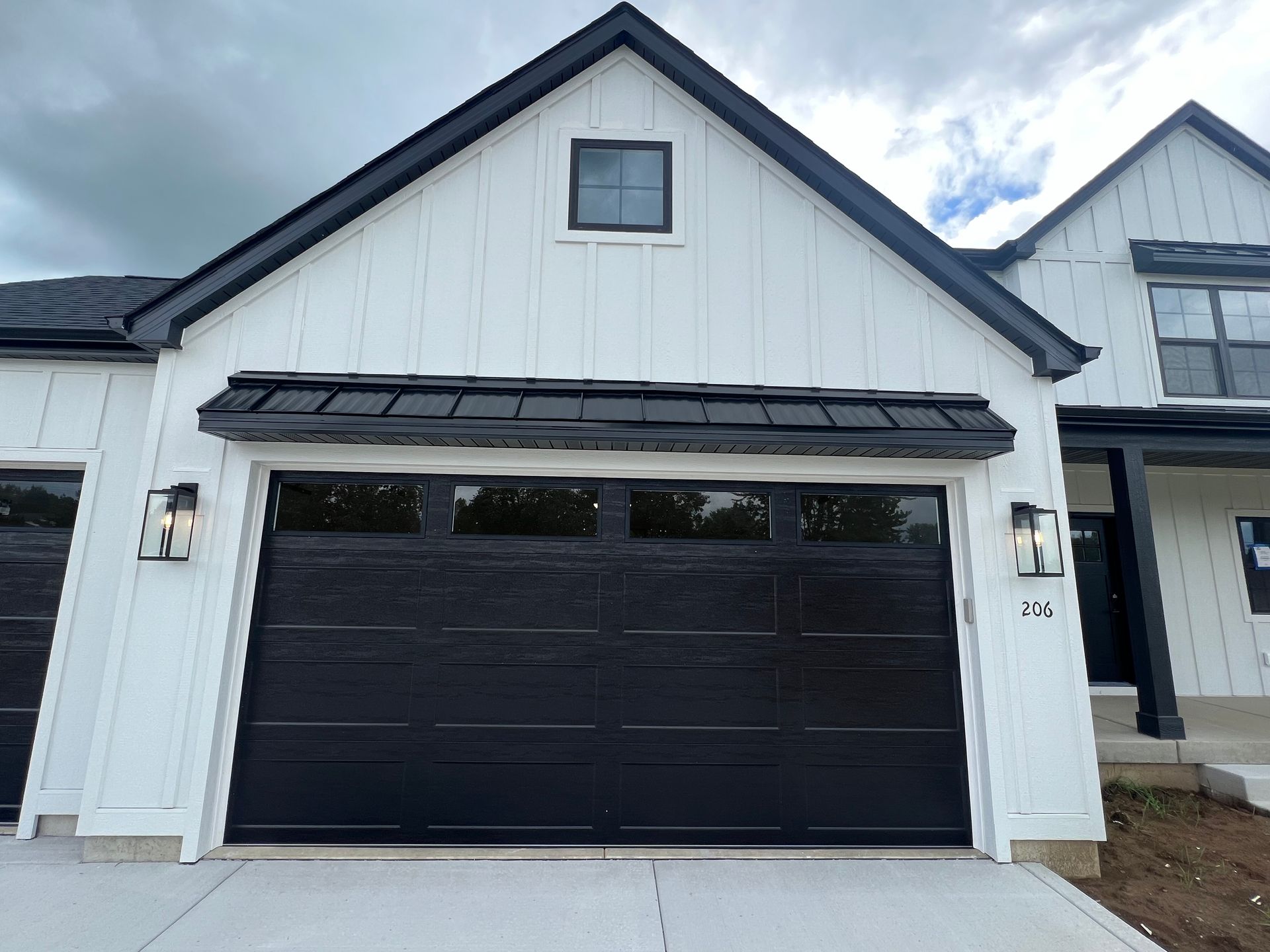 Black garage door on a white house exterior with a small upper window and gray roofline