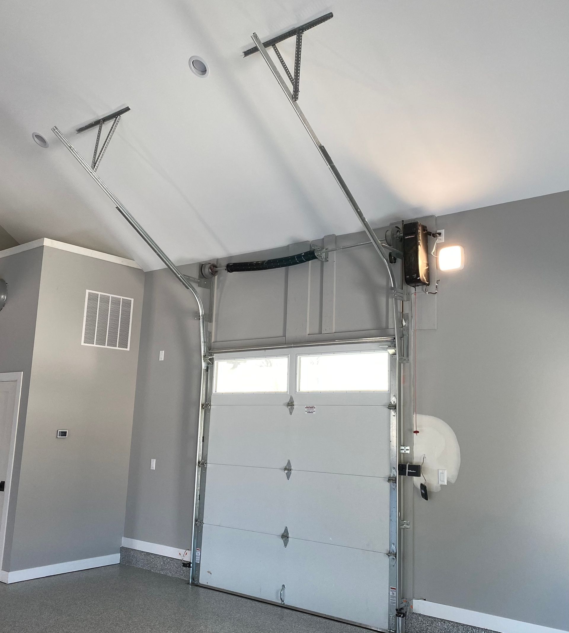 Interior of a garage with a white overhead door, gray walls, and ceiling-mounted garage door opener tracks
