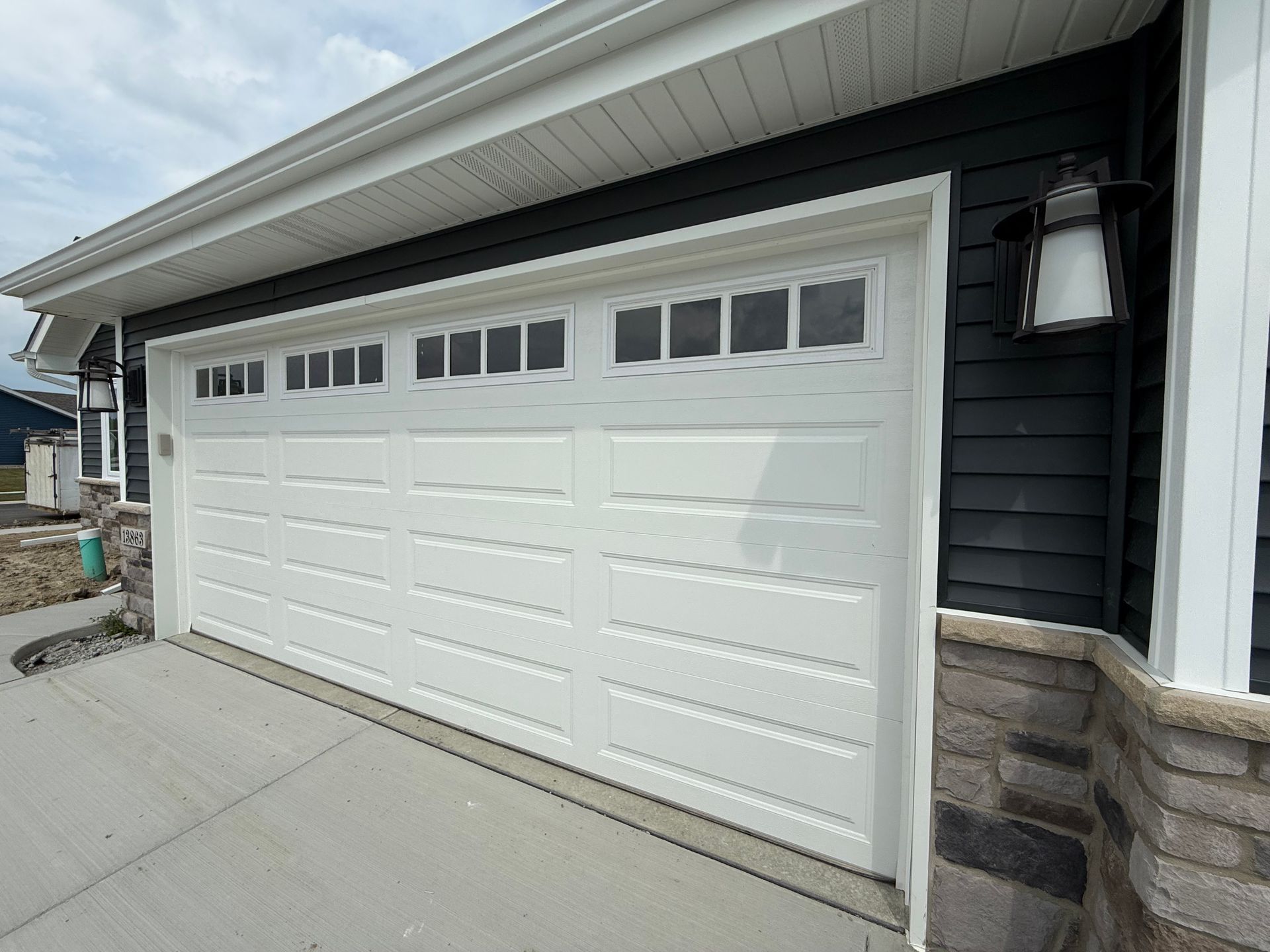 White garage door on a dark-sided house with stone trim and concrete driveway