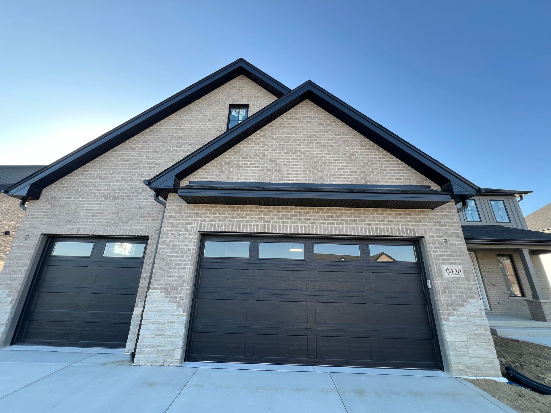 Modern brick house exterior with black garage doors and a snow-covered driveway