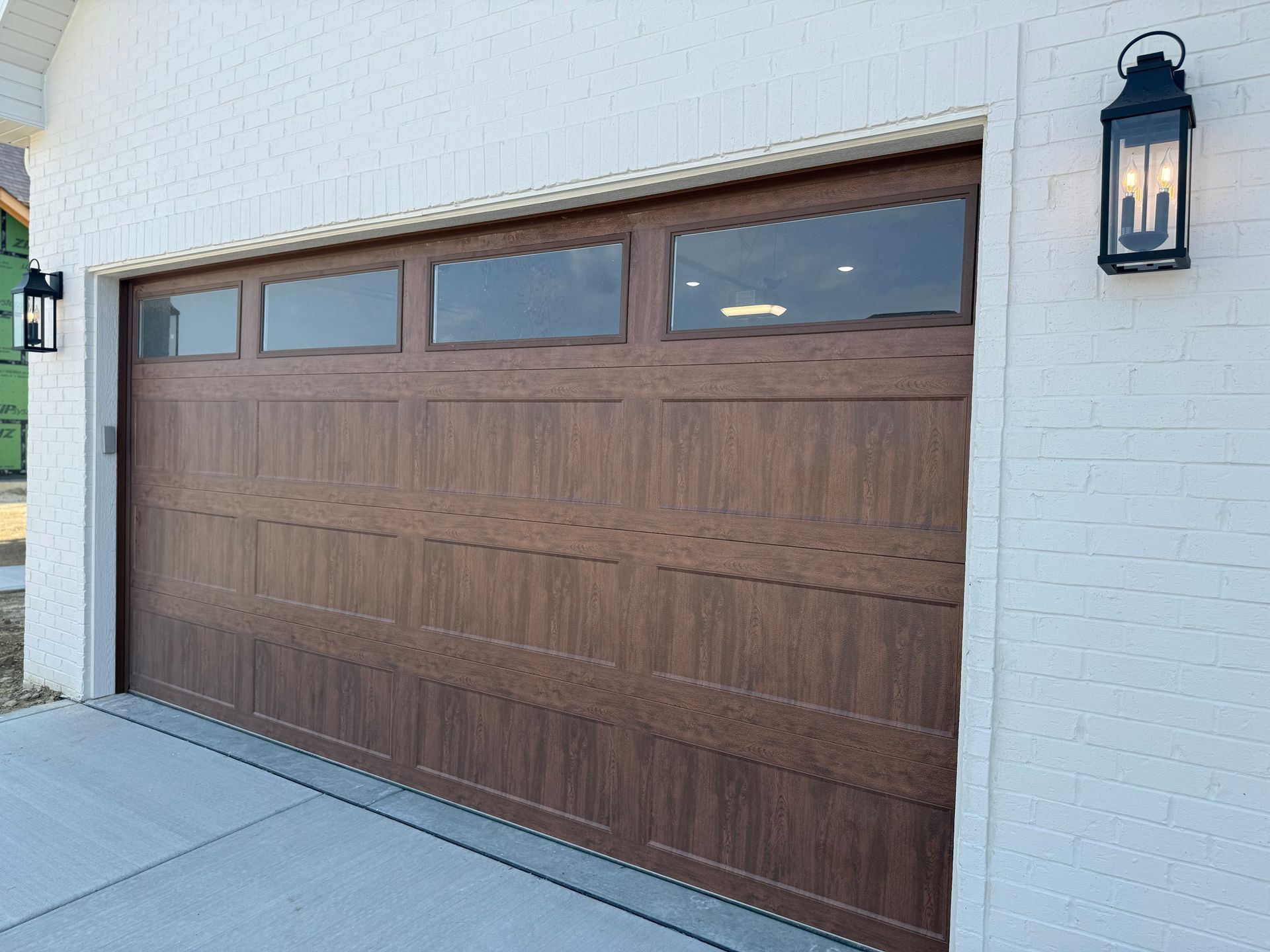 Wooden garage door with small windows on a white brick house exterior