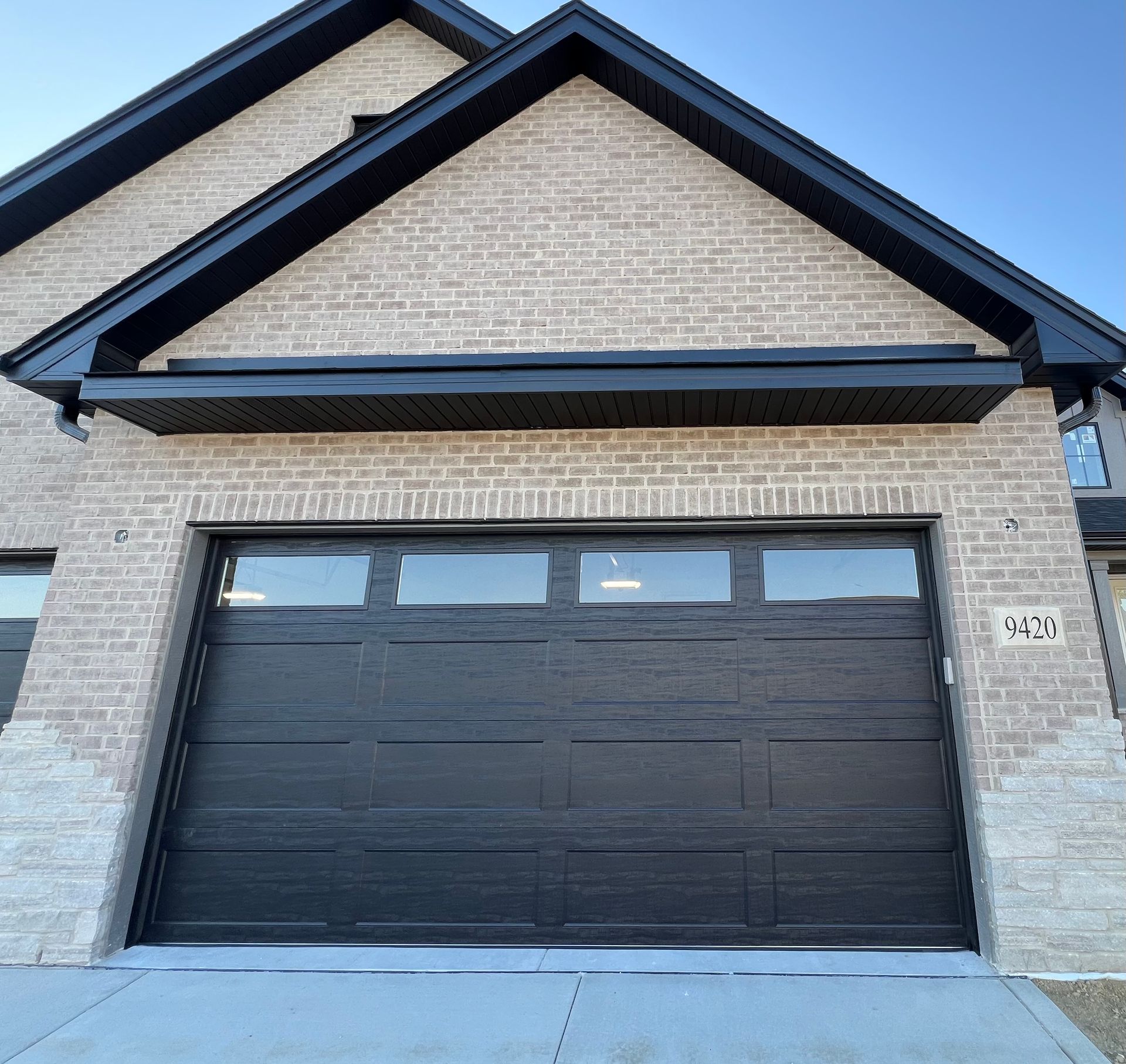 Modern brick house exterior with a black double garage door and peaked roof