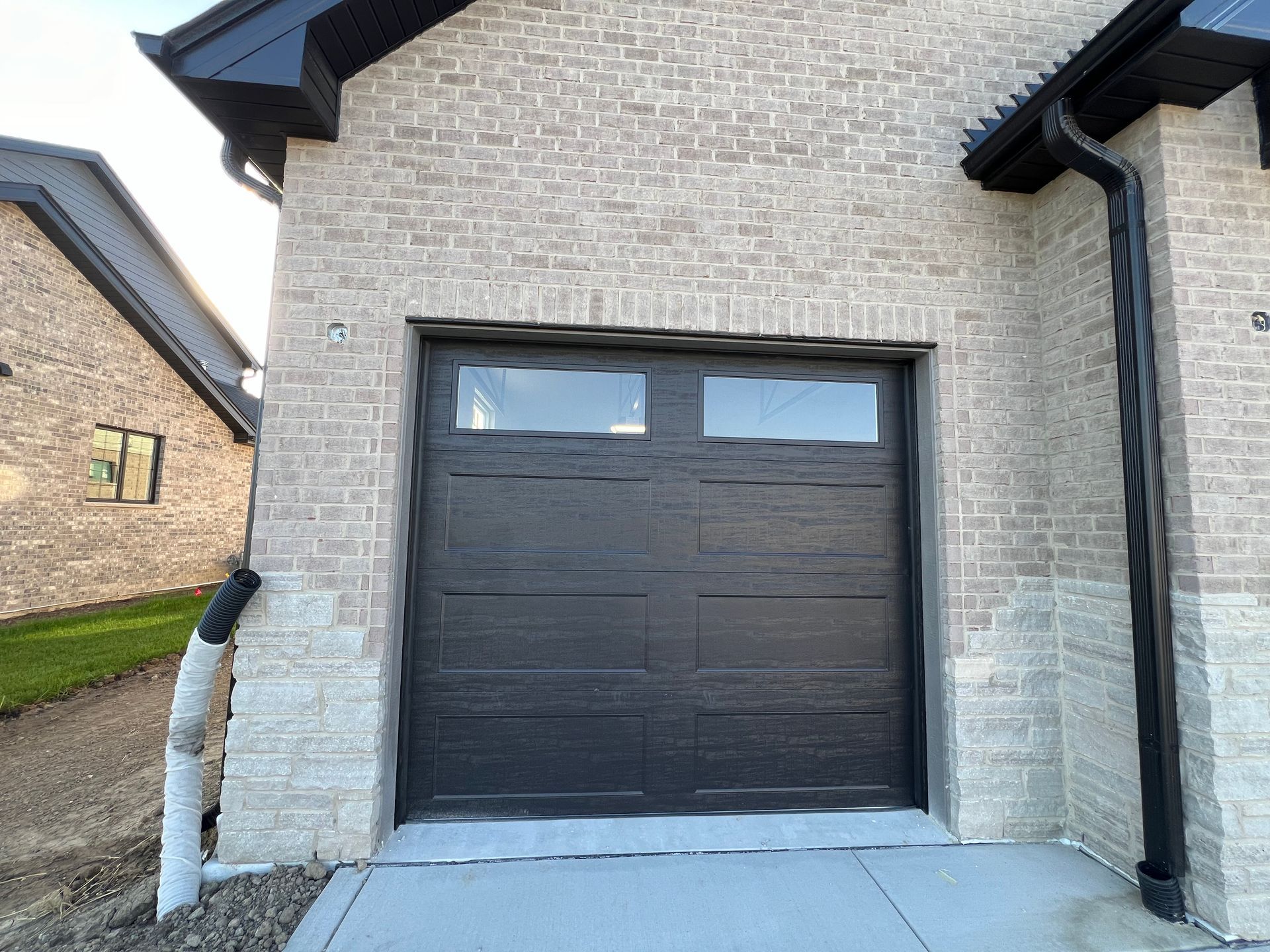Black garage door on a beige brick house with narrow windows above and a side downspout.
