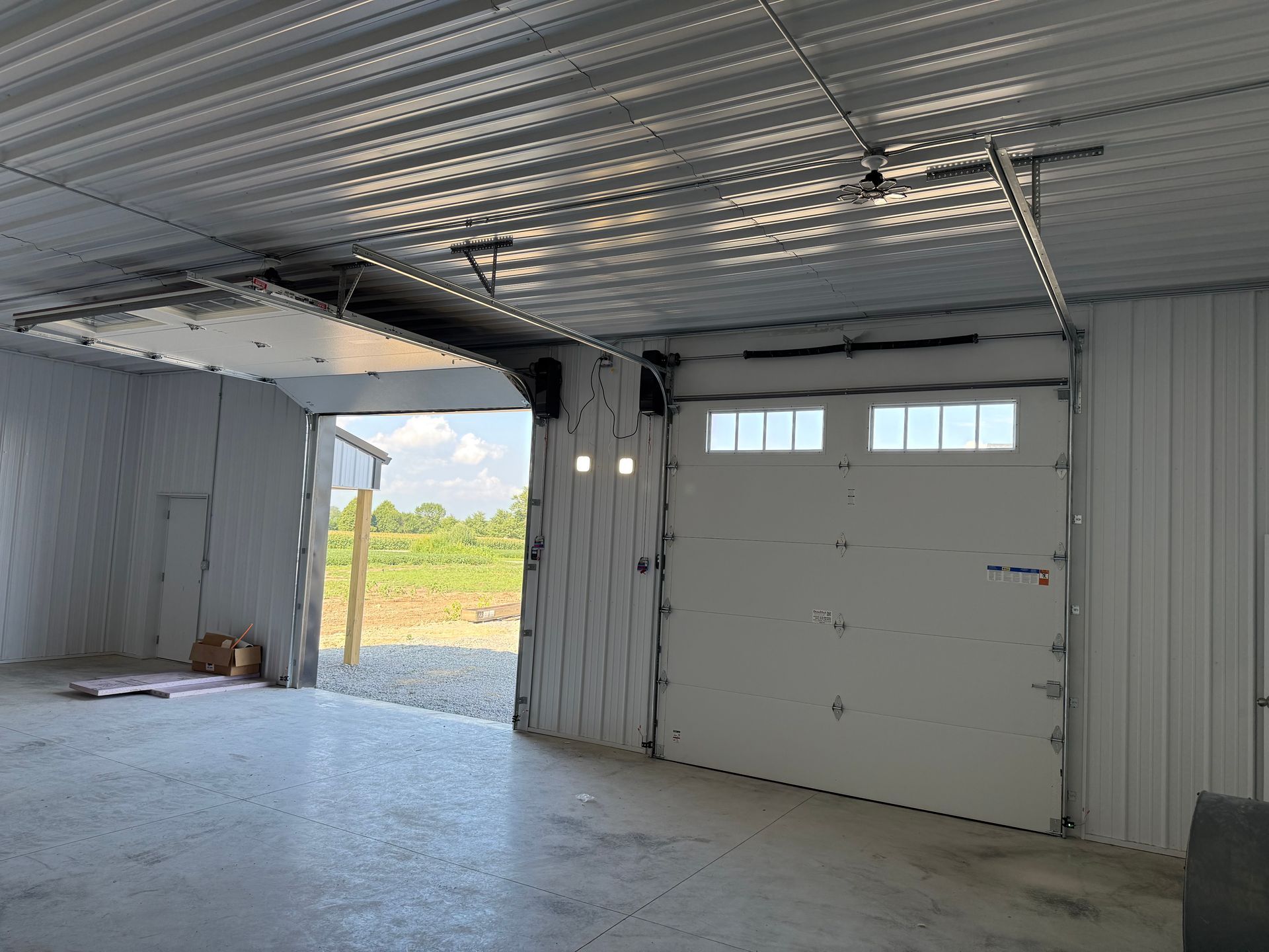 Empty garage with white walls, concrete floor, and an open doorway showing grass outside.