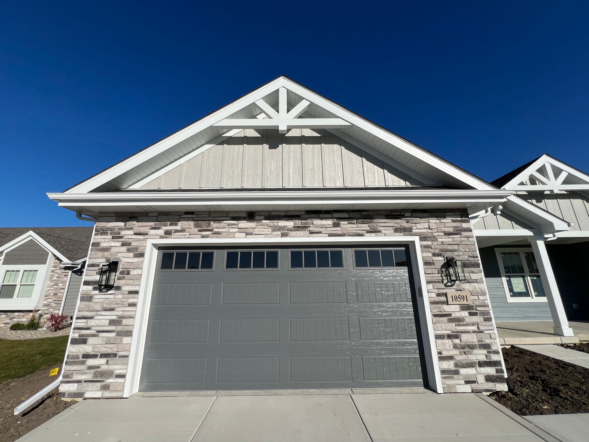 Stone-and-gray garage on a suburban house with a peaked roof under a clear blue sky