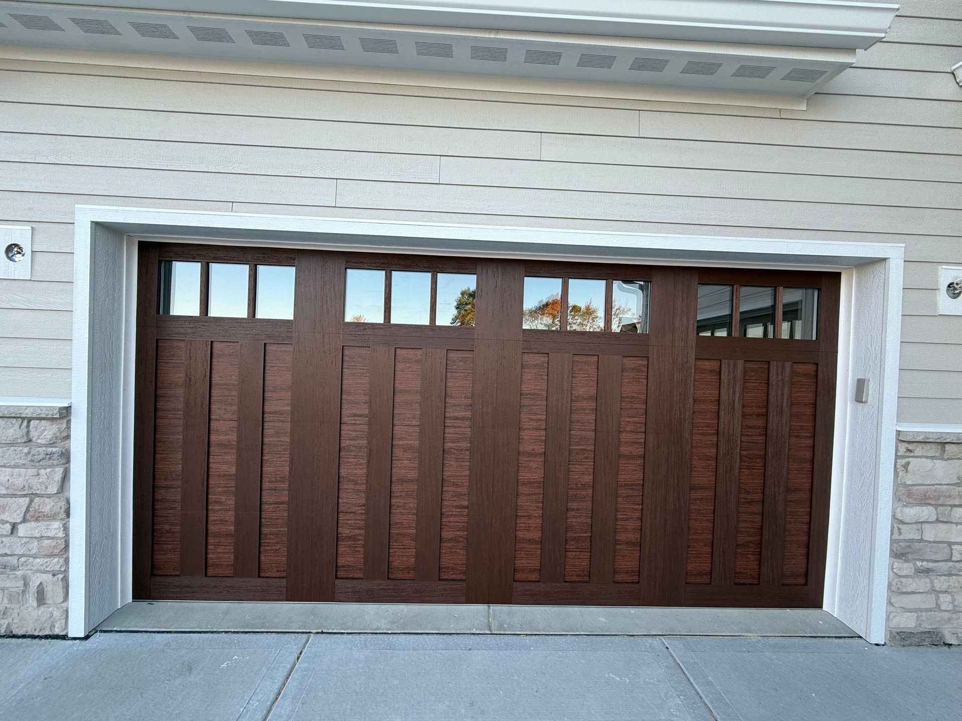 Brown wooden garage door with small window panes in a stone-and-siding house exterior