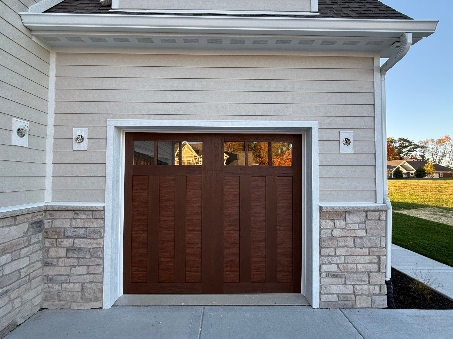 Wood-front garage doors on a beige house with stone trim and white framing