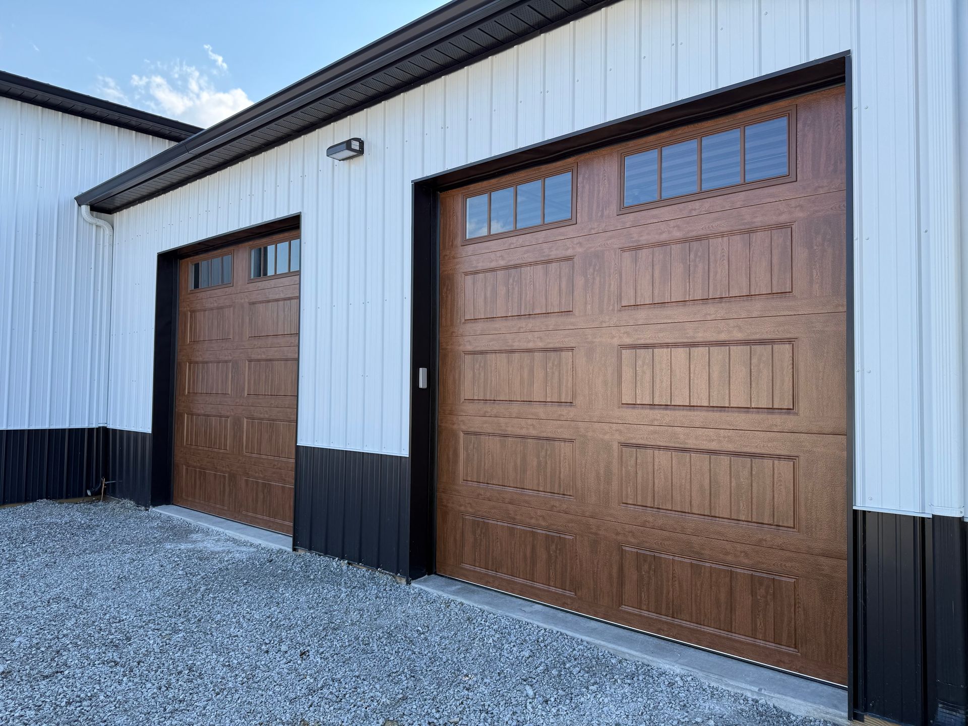 White metal building exterior with two brown garage doors and gravel foreground