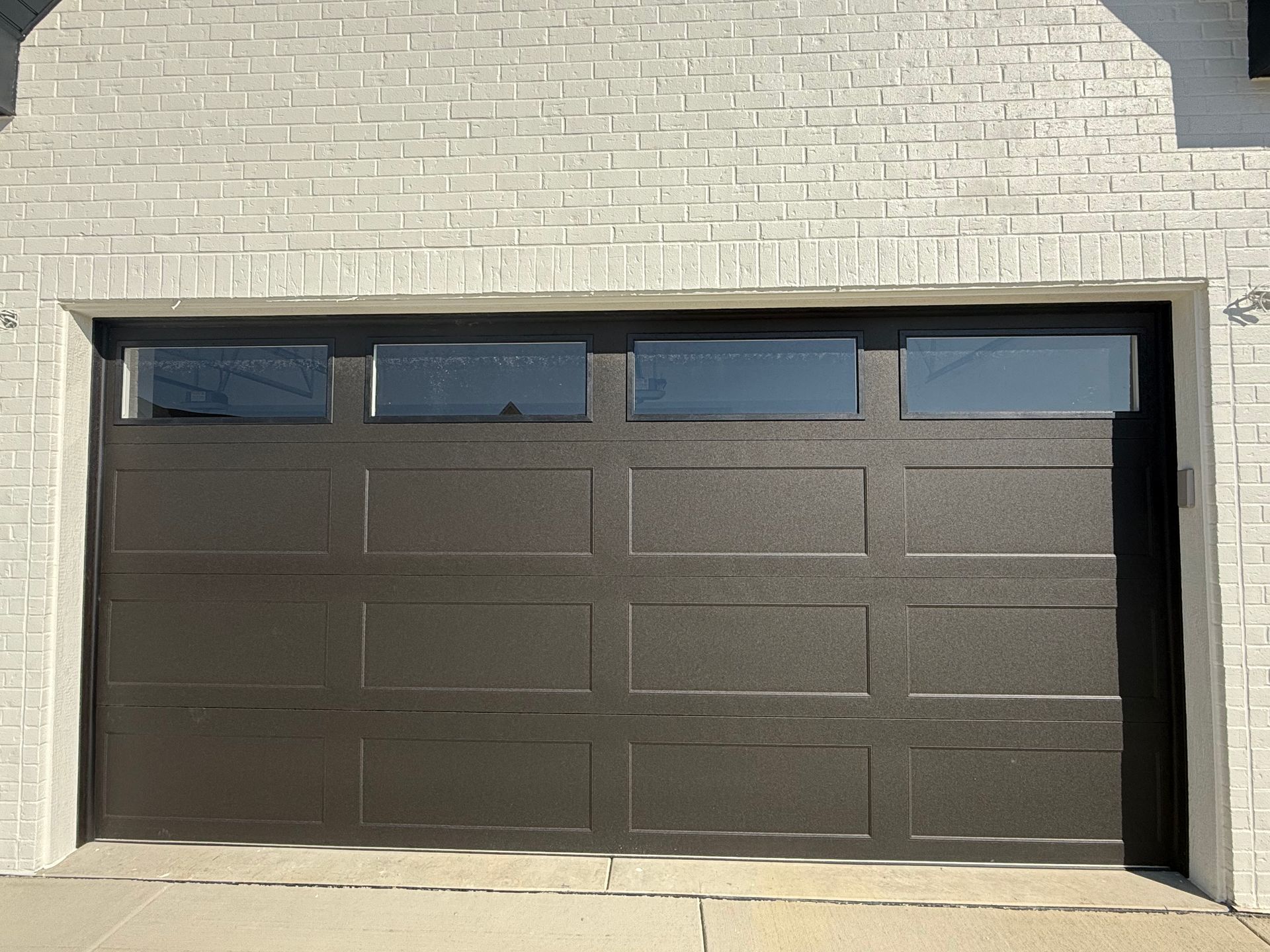Dark brown garage door set in a light brick exterior wall with four small windows along the top.