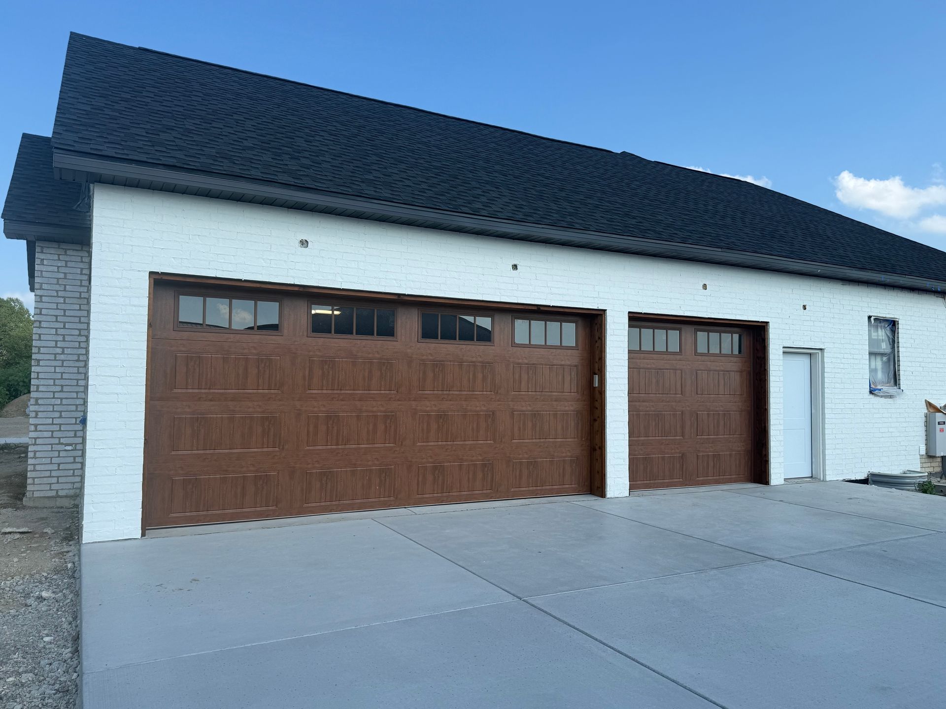 White house with two brown garage doors and a steep dark roof, viewed from a sloped concrete driveway.