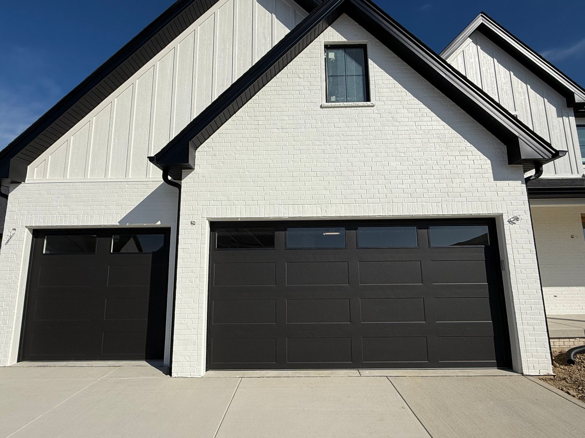 White house exterior with black garage doors and gabled roof in bright sunlight