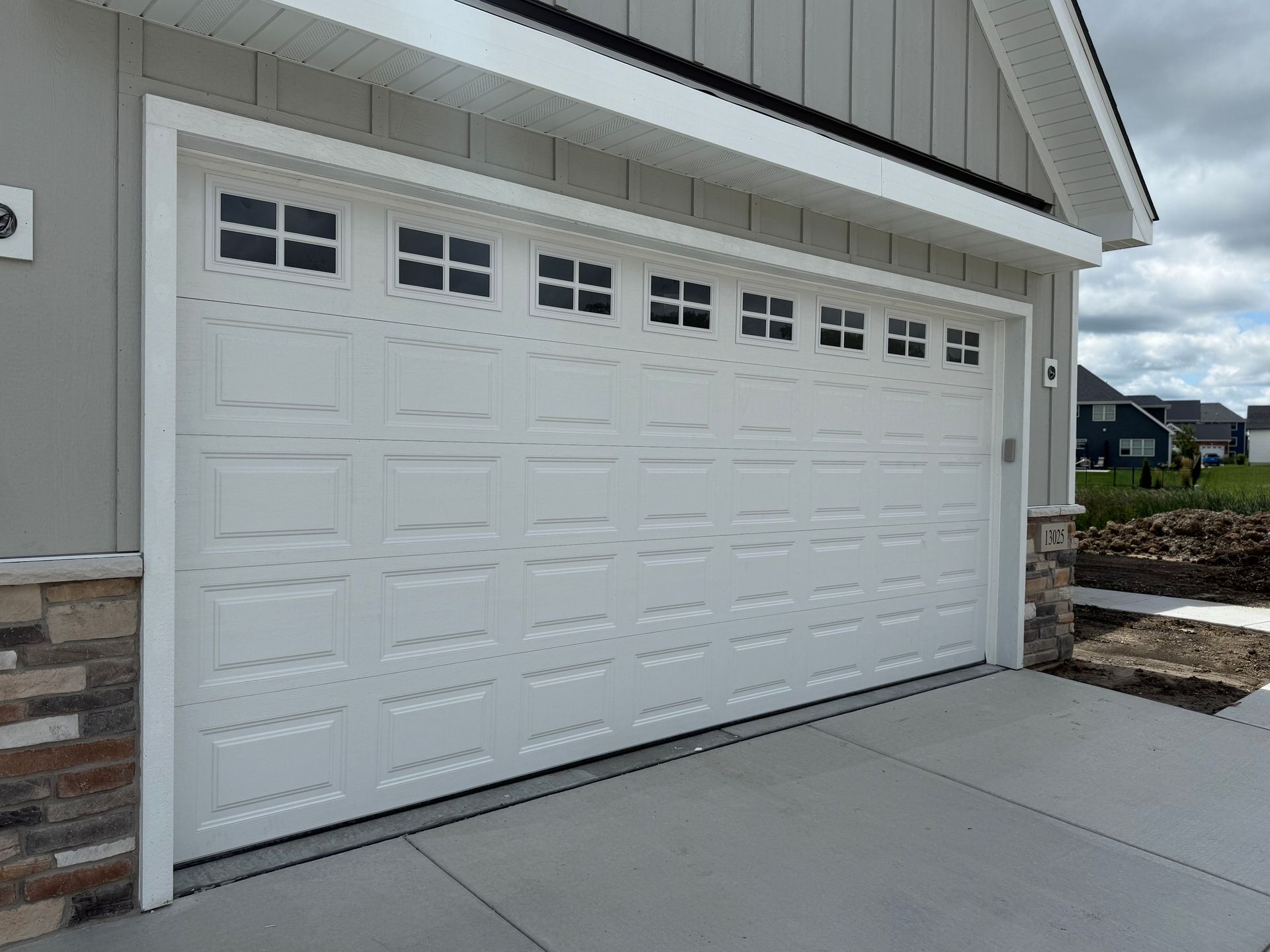 White two-car garage door on a beige house with a concrete driveway and side steps