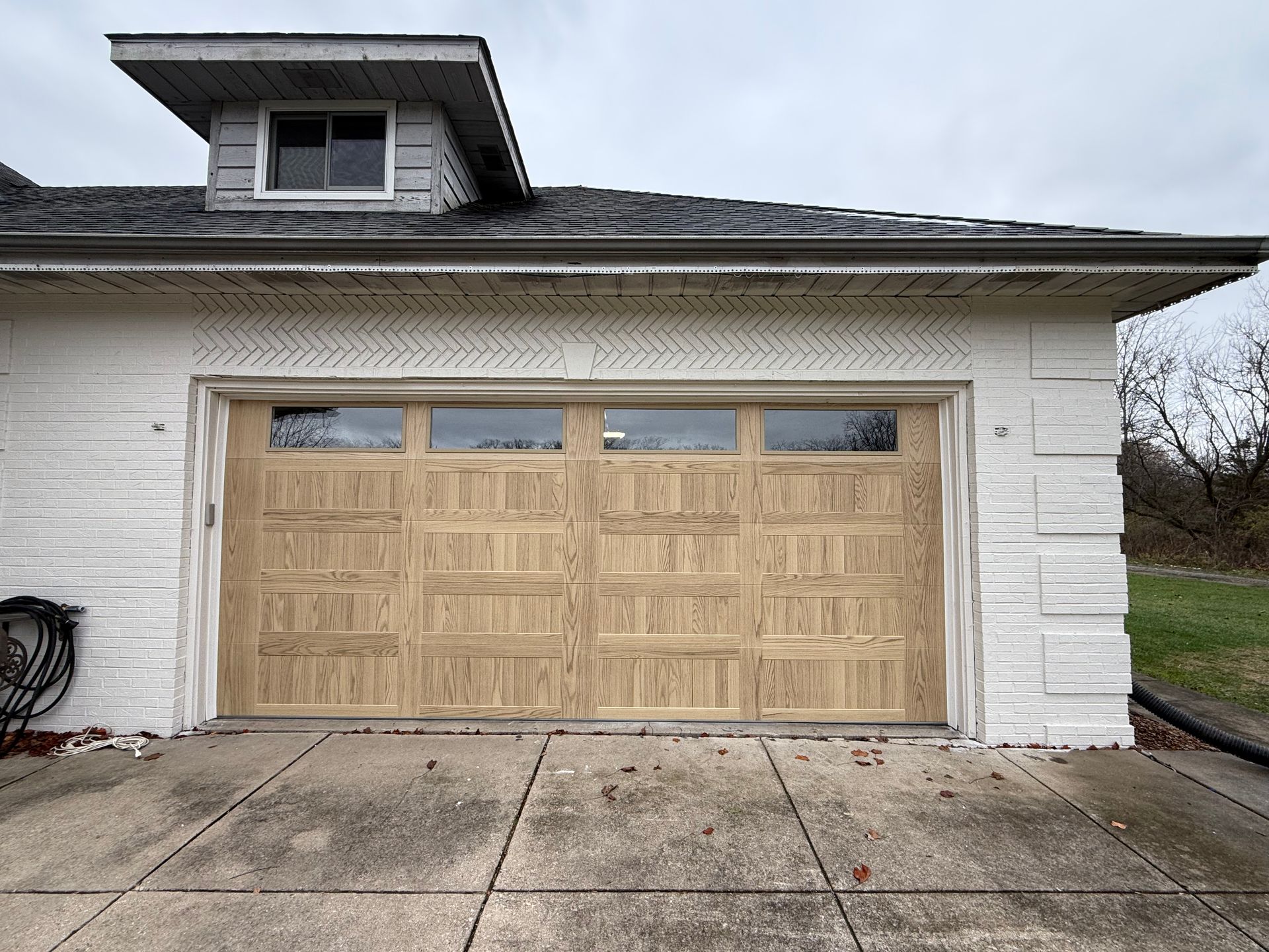 White two-car garage with tan wooden door and driveway in front of a house